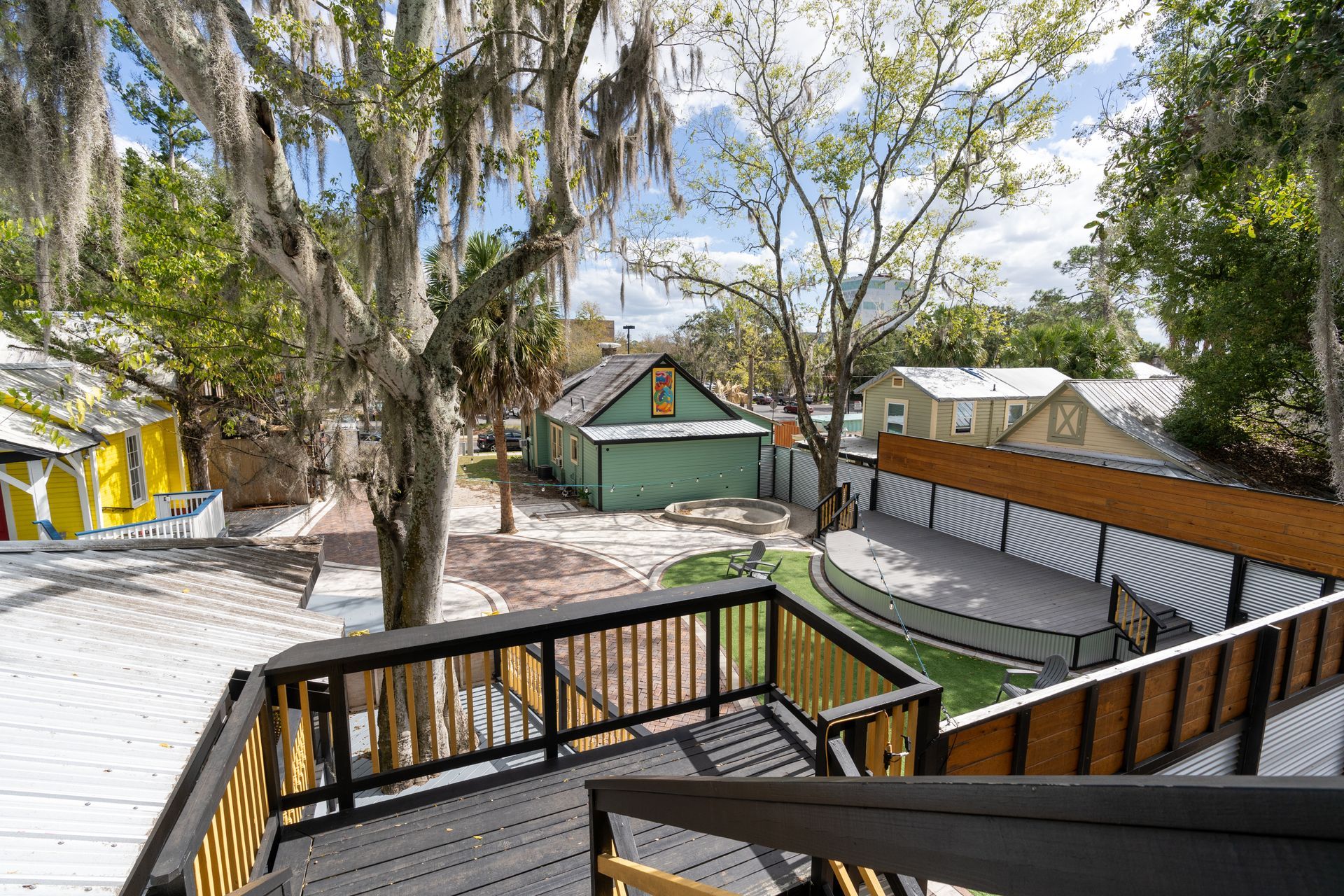 Exterior view of a backyard with a deck, trees, and buildings in various colors.