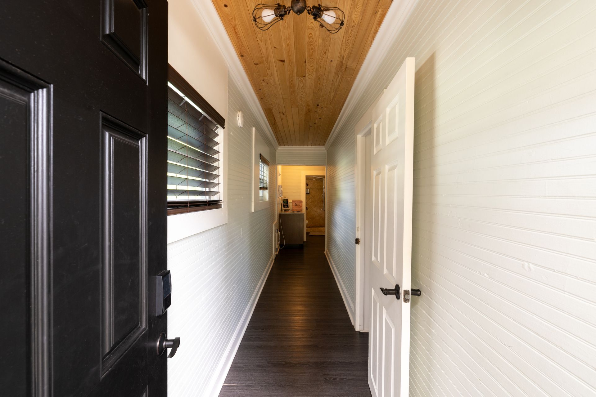 Hallway with dark wooden floor, wood-paneled ceiling, white walls, and open black door.