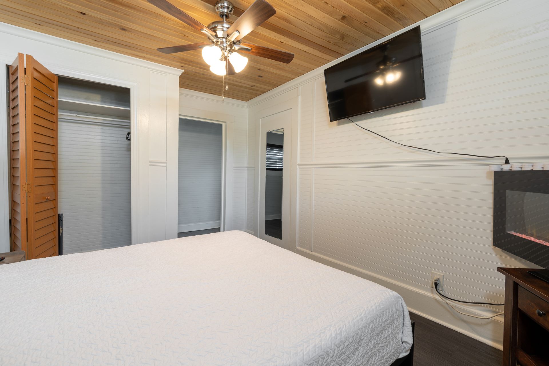 Bedroom with white walls, wood ceiling, bed, closet, TV, and fireplace.