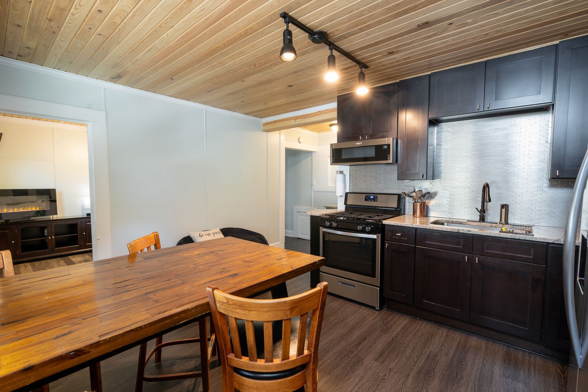 Kitchen with dark cabinets, stainless steel appliances, and a wooden dining table.