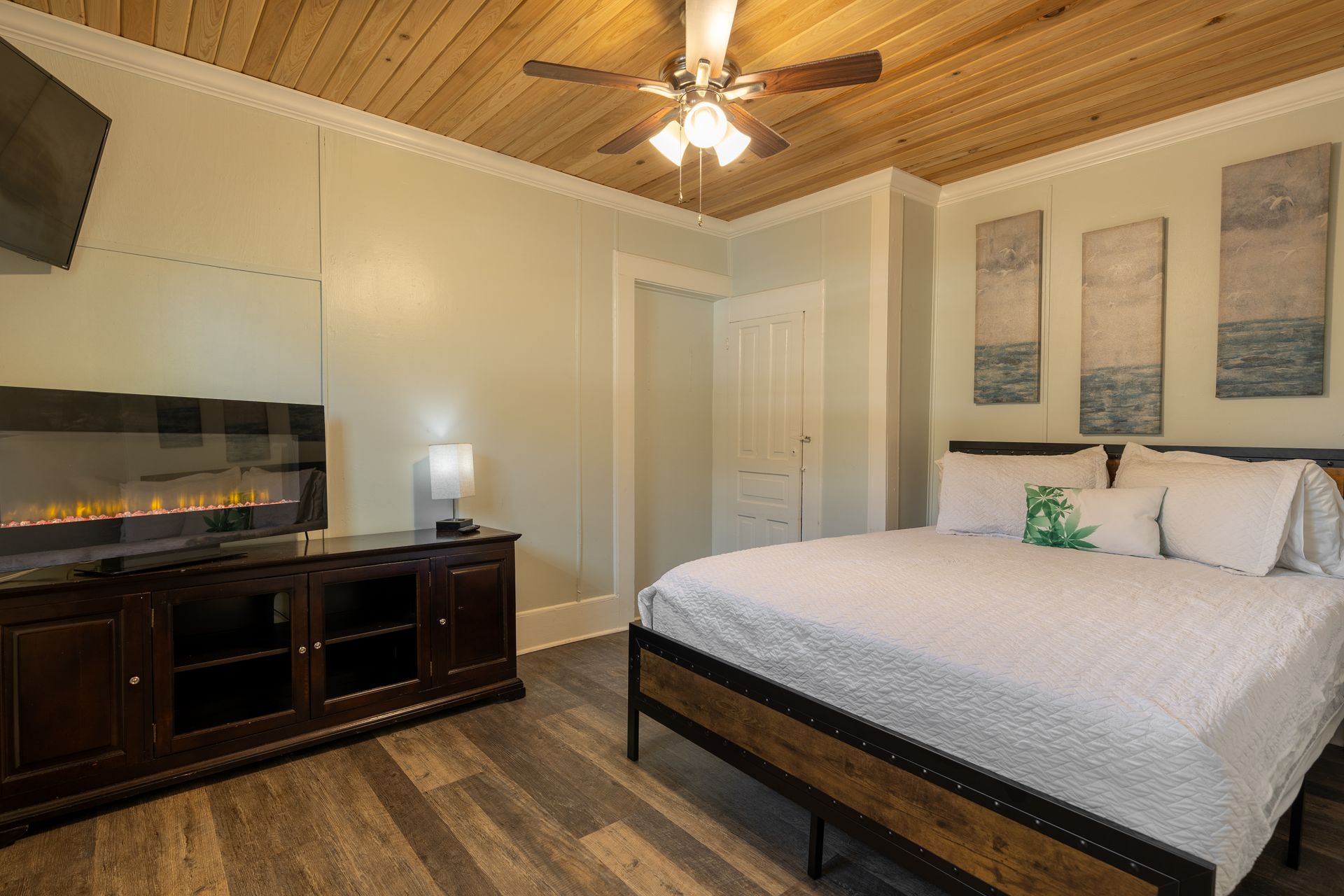 Bedroom with bed, fireplace, TV, wood ceiling, and artwork.