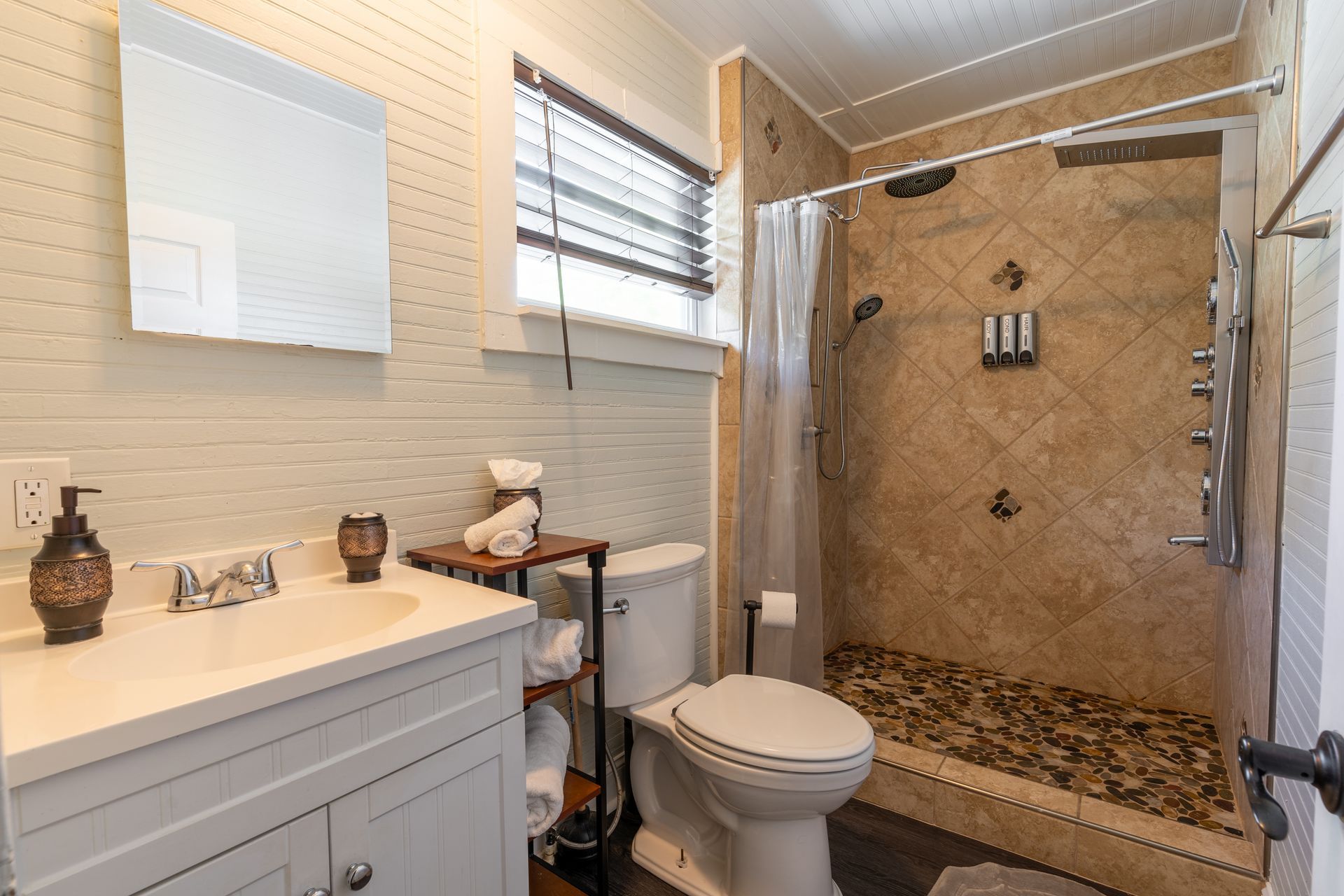 Bathroom with white vanity, toilet, and tiled shower. Light beige walls.