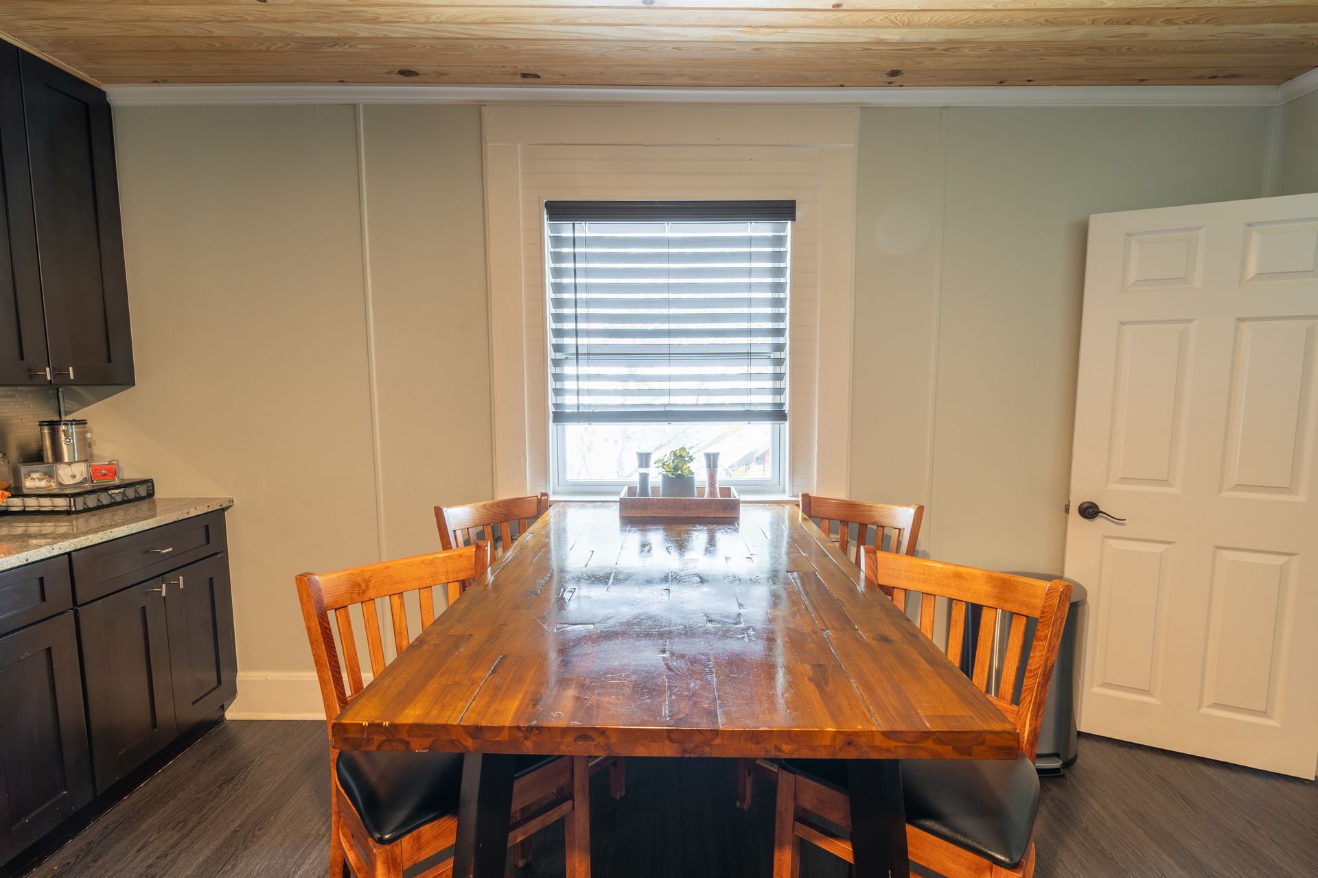 Dining room with wooden table, chairs, window with blinds, and door.