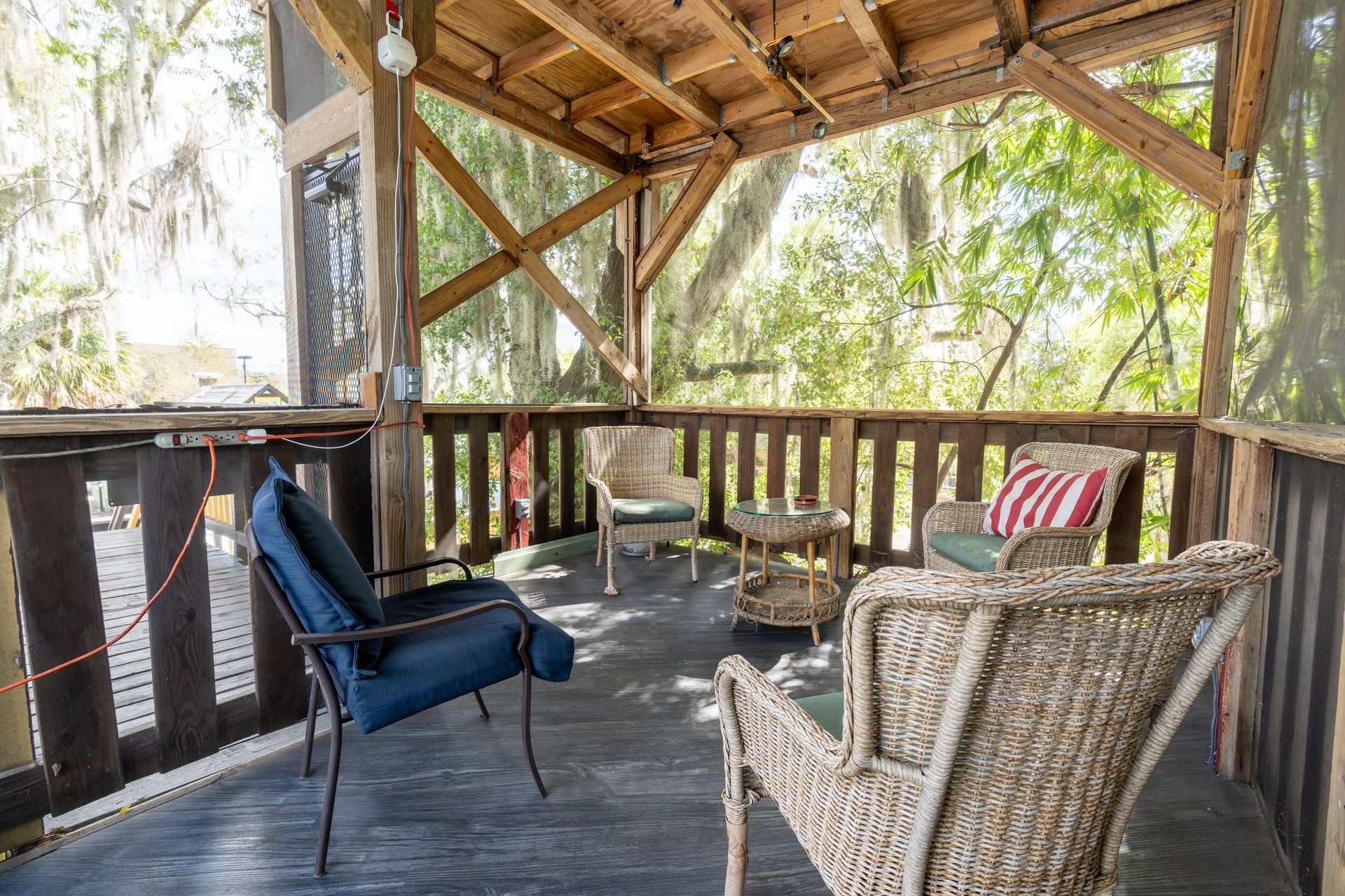 Covered porch with chairs, overlooking a wooded area. Blue, white, and red pillows.