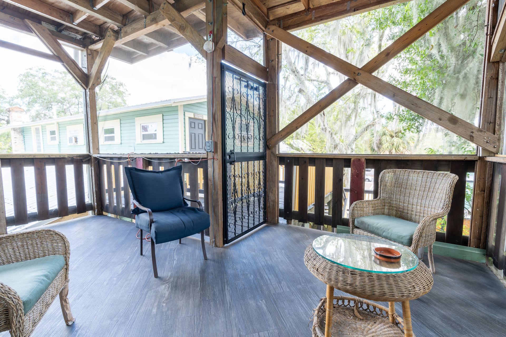 Covered porch with seating; wicker chairs, glass-topped table, and wooden railings.