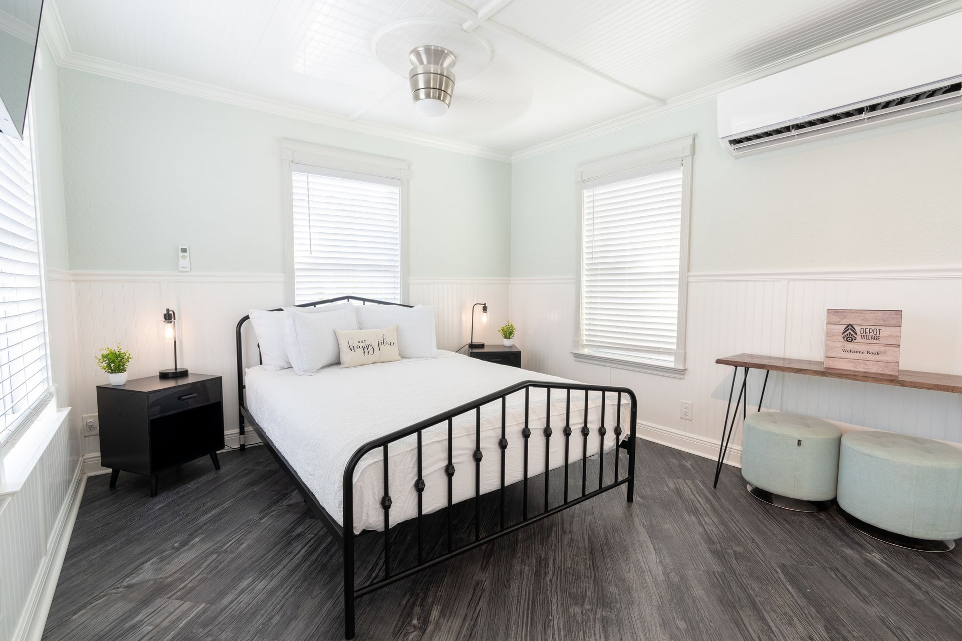 Bedroom with a bed, nightstands, windows, and a bench. The walls are light blue and white.