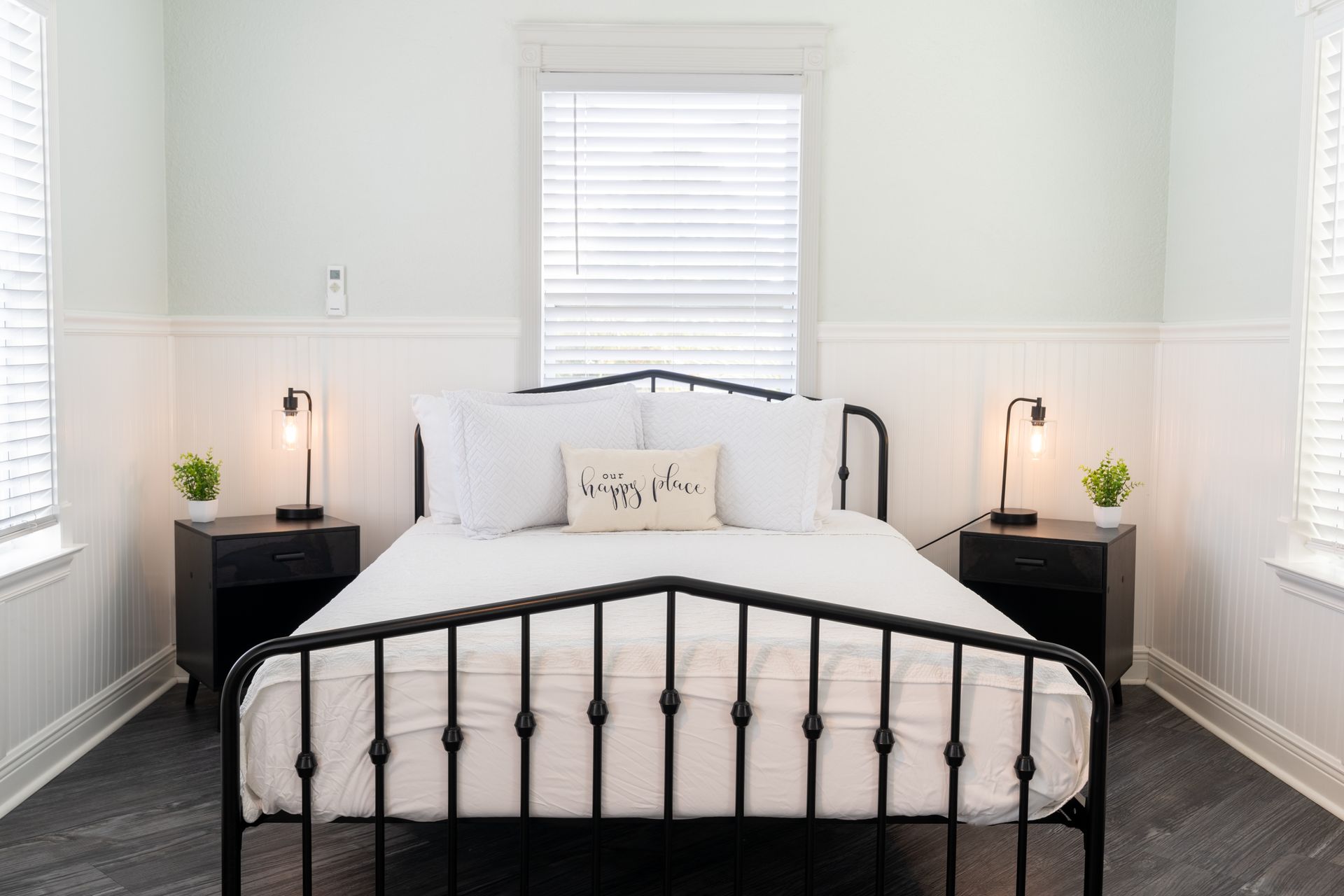 Bedroom with black metal bed, bedside tables, lamps, and white walls.