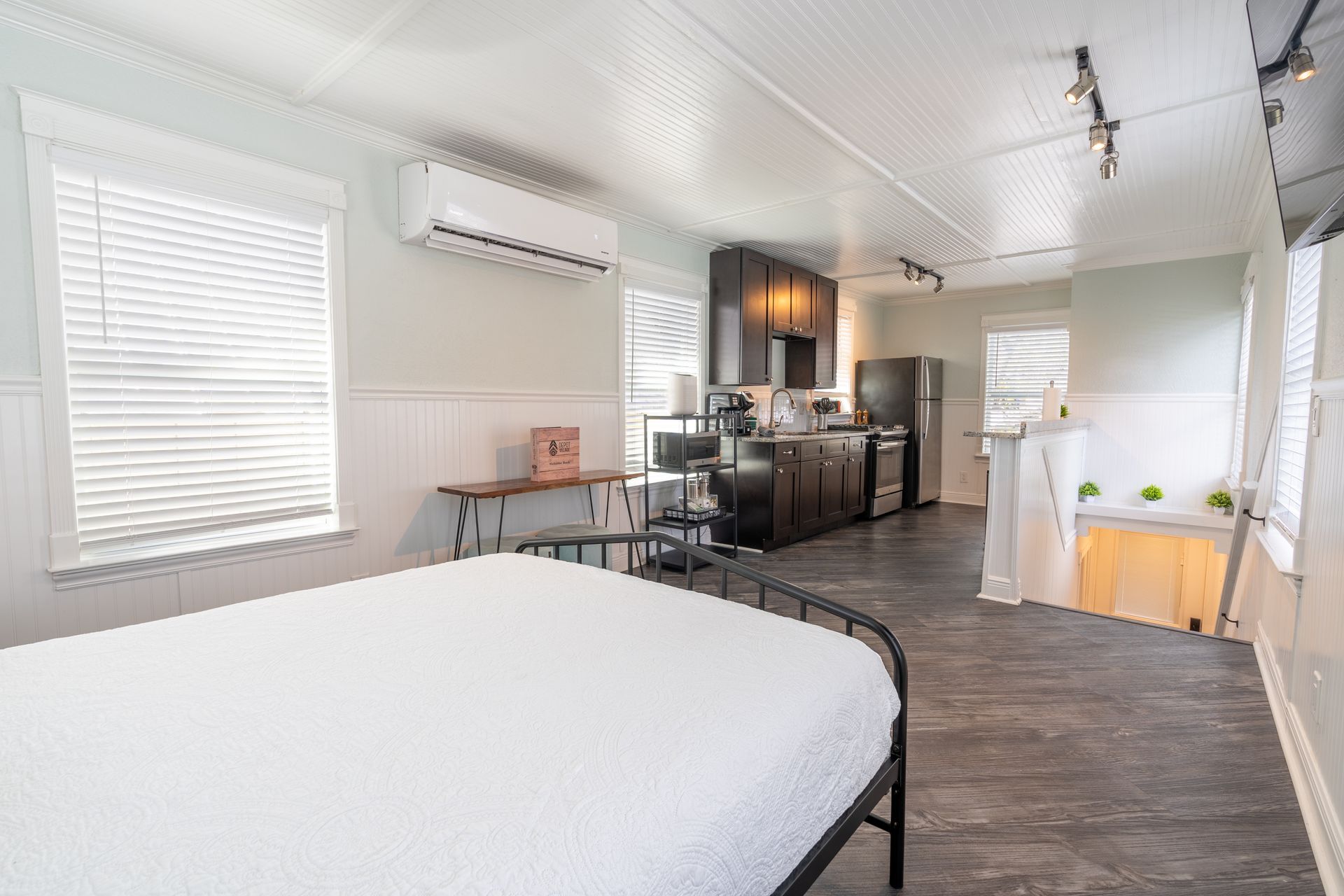 Studio apartment with bed, kitchenette, and air conditioning unit.