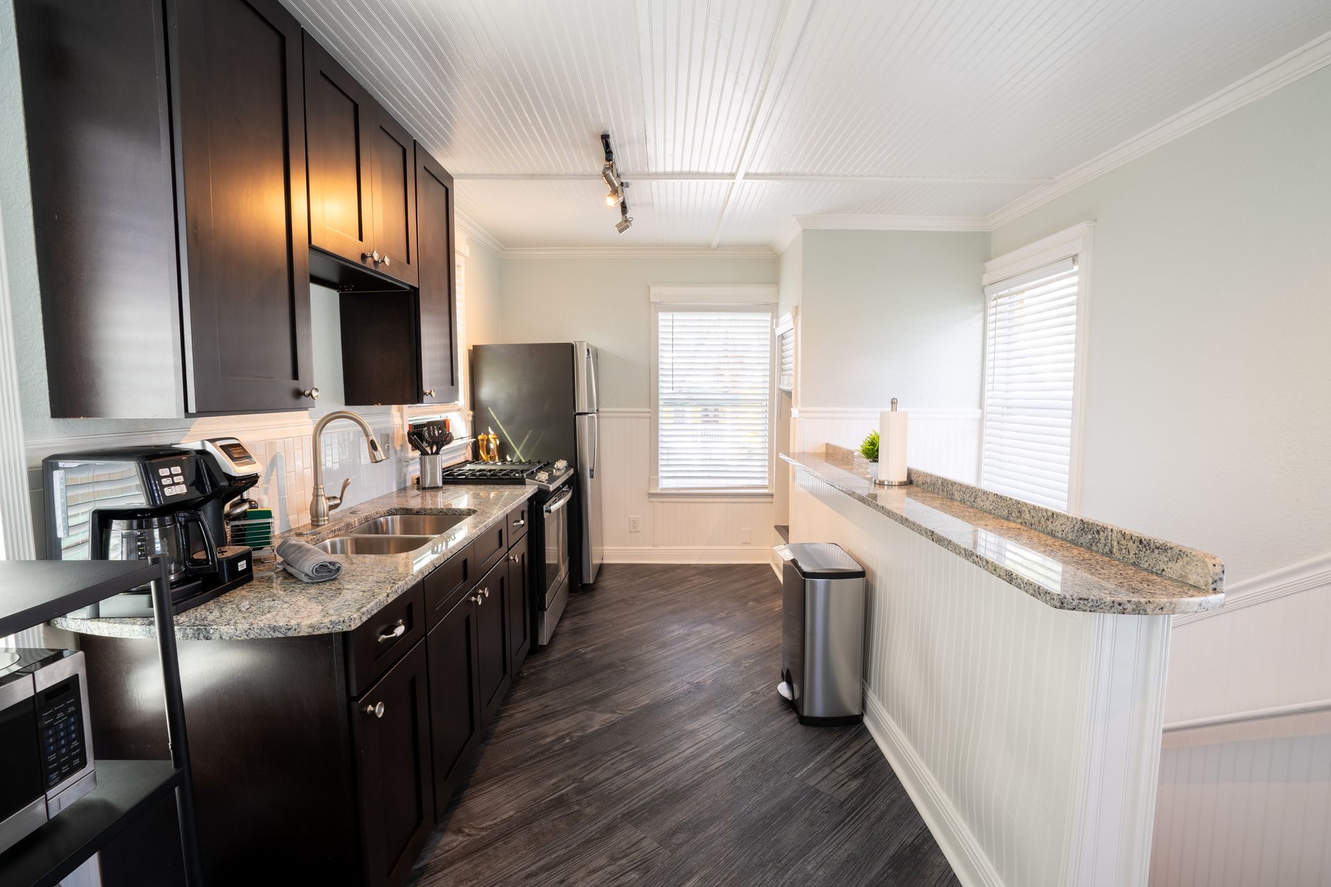 Dark cabinetry kitchen with stainless appliances, granite counters, and wood-look flooring.