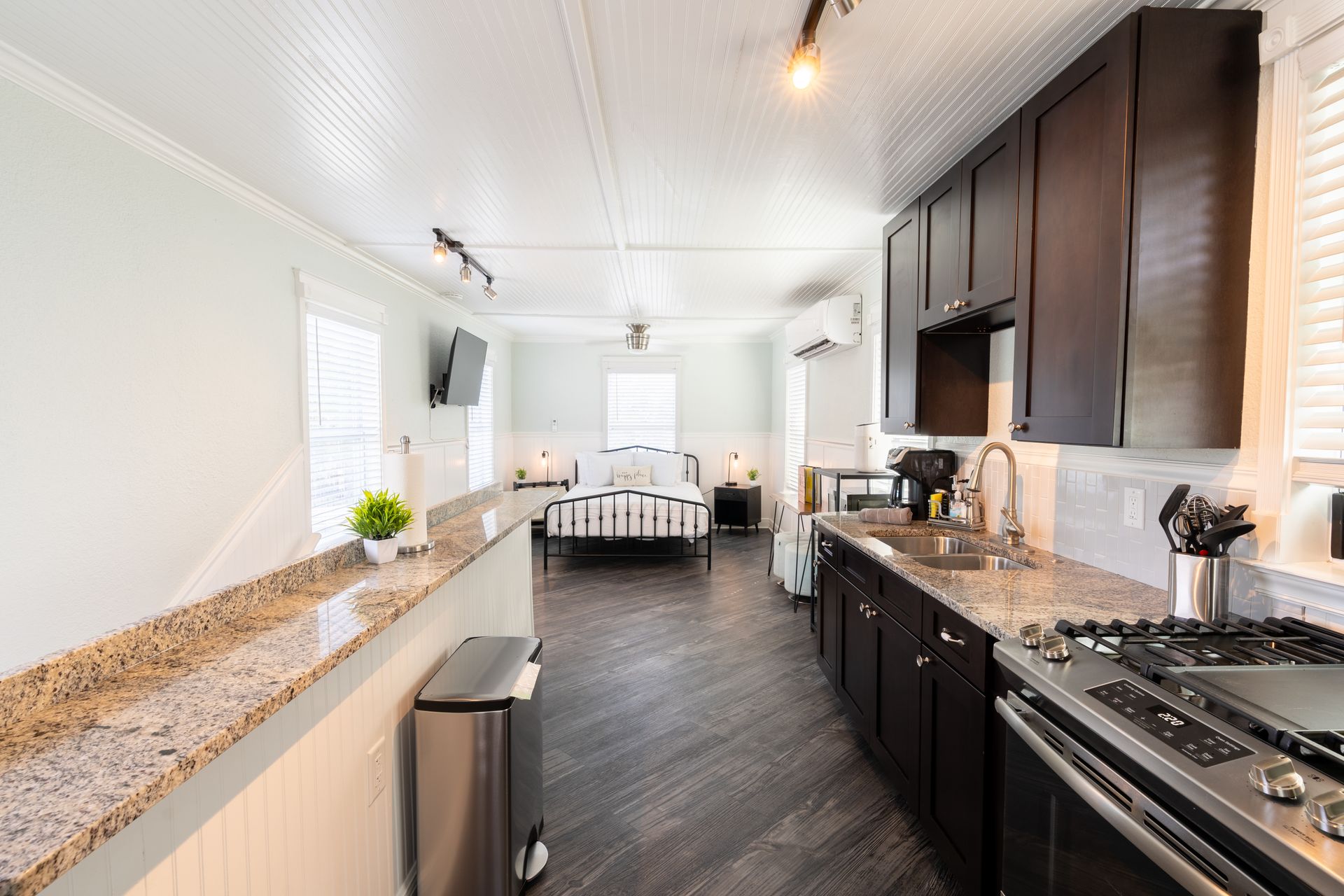 Interior of a studio apartment, featuring a kitchen, bed, and living space with wood and light-colored walls.