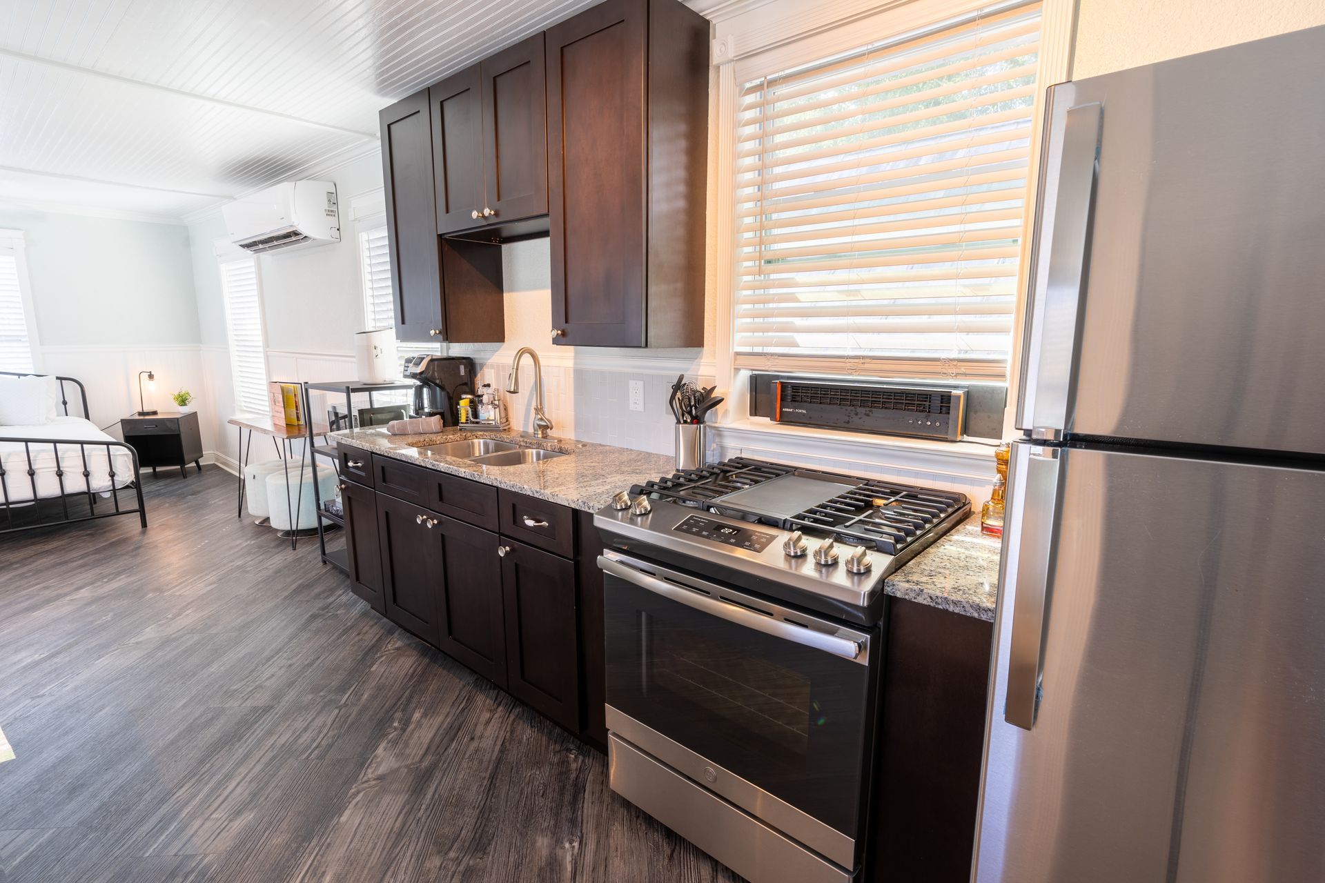 Small kitchen with dark cabinets, stainless steel appliances, and a window with blinds.