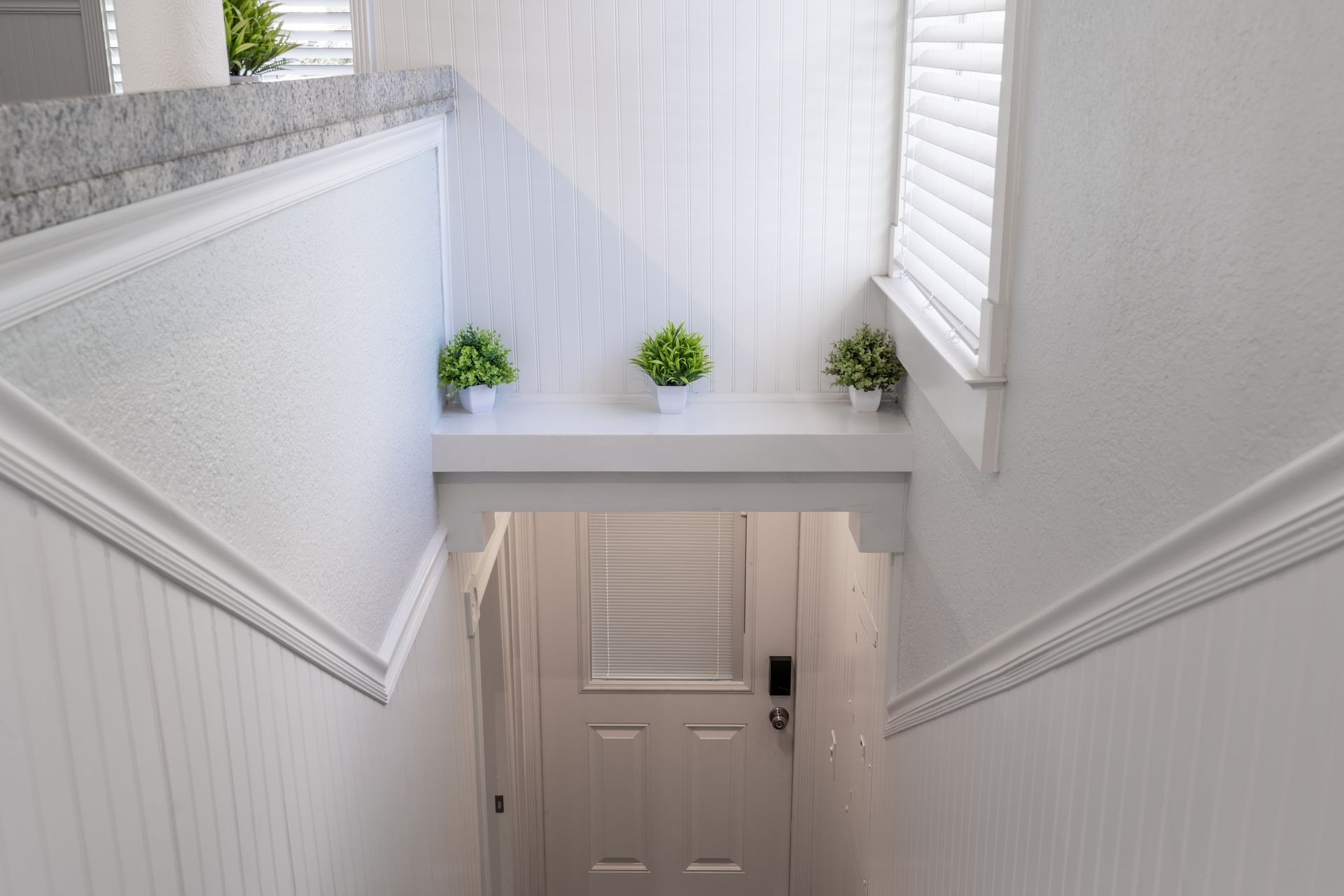 White staircase leading to a door, with small plants on a ledge.