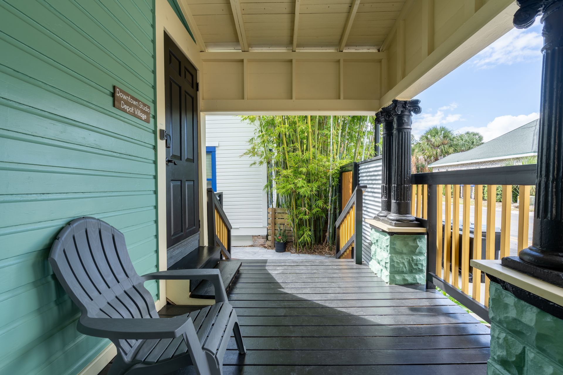 A gray Adirondack chair sits on a turquoise porch with black columns and railings.
