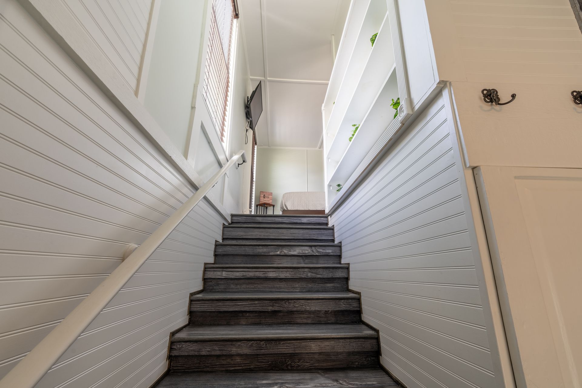 Staircase with gray steps and white paneled walls, leading upwards.