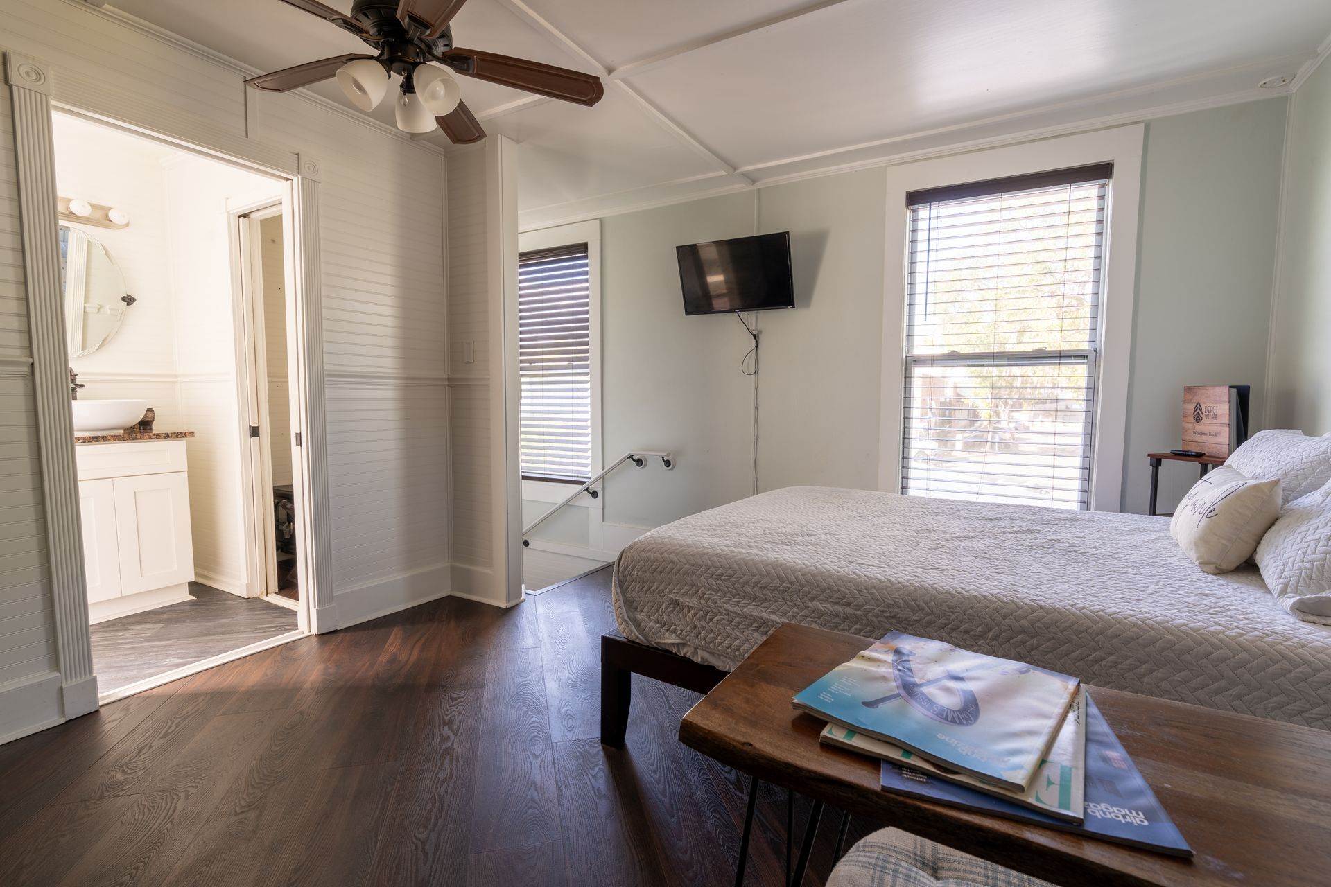 Bedroom with dark hardwood floors, white walls, and a queen bed. A TV is mounted above the bed.