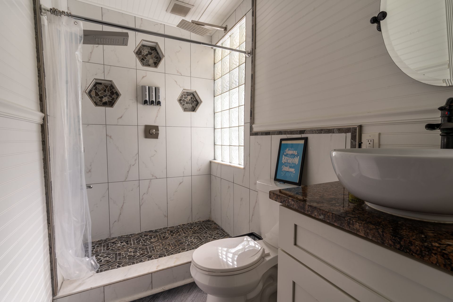 Bathroom with white tile shower, pebble floor, glass block window, and white sink.