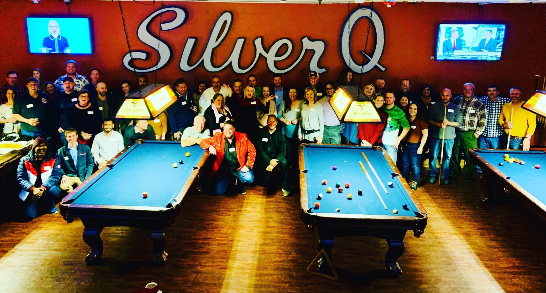 Large group of people pose around pool tables at a bar called Silver Q.