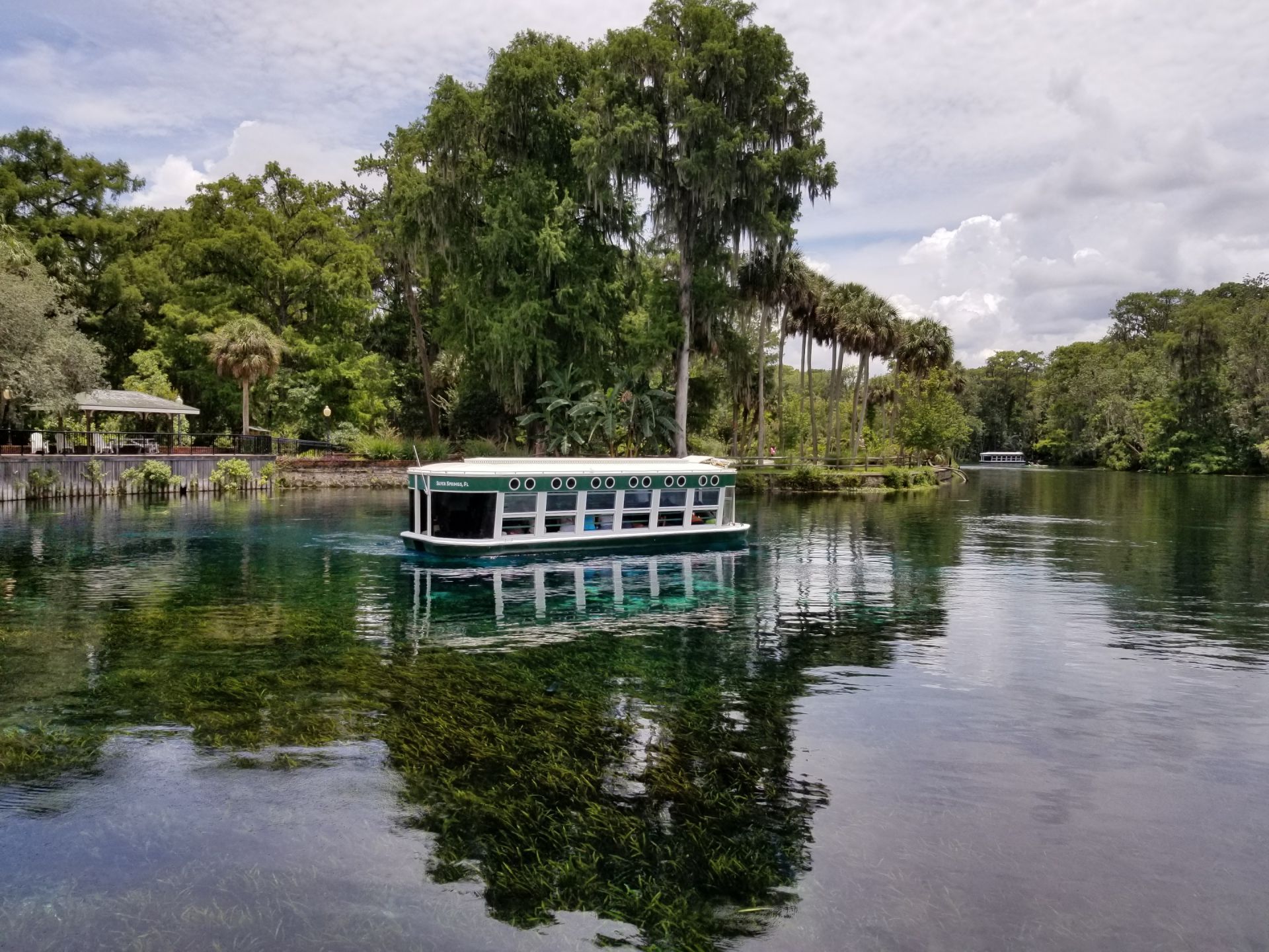 A tour boat on a clear, turquoise spring with lush green trees in the background.