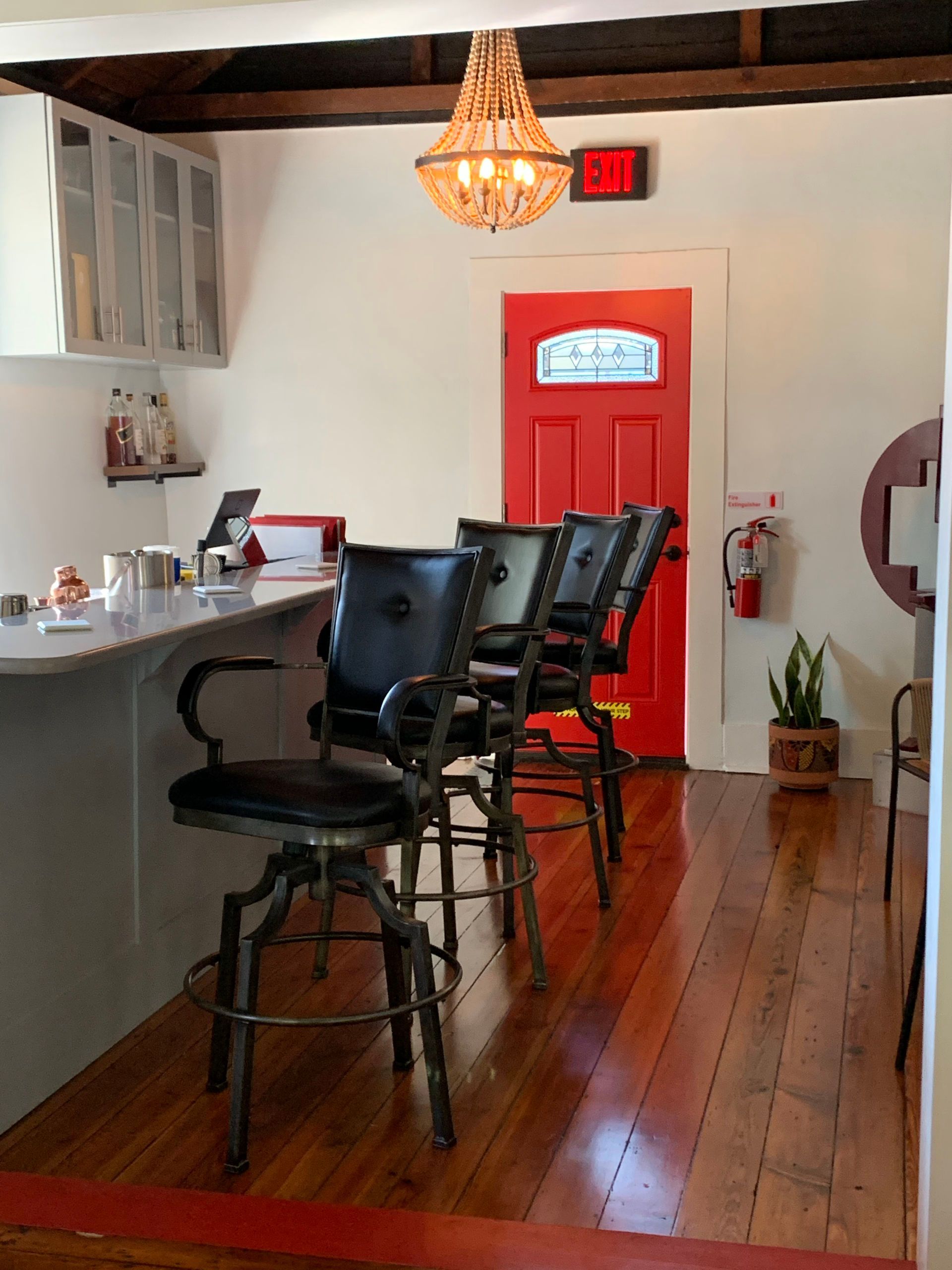 Bar with black swivel stools, white counter, red door, and wood floor.