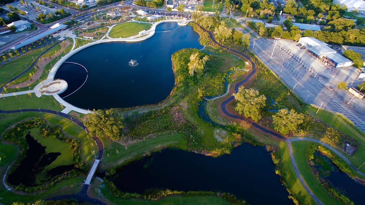 Aerial view of a park with a lake, green spaces, walking paths, and a parking lot.