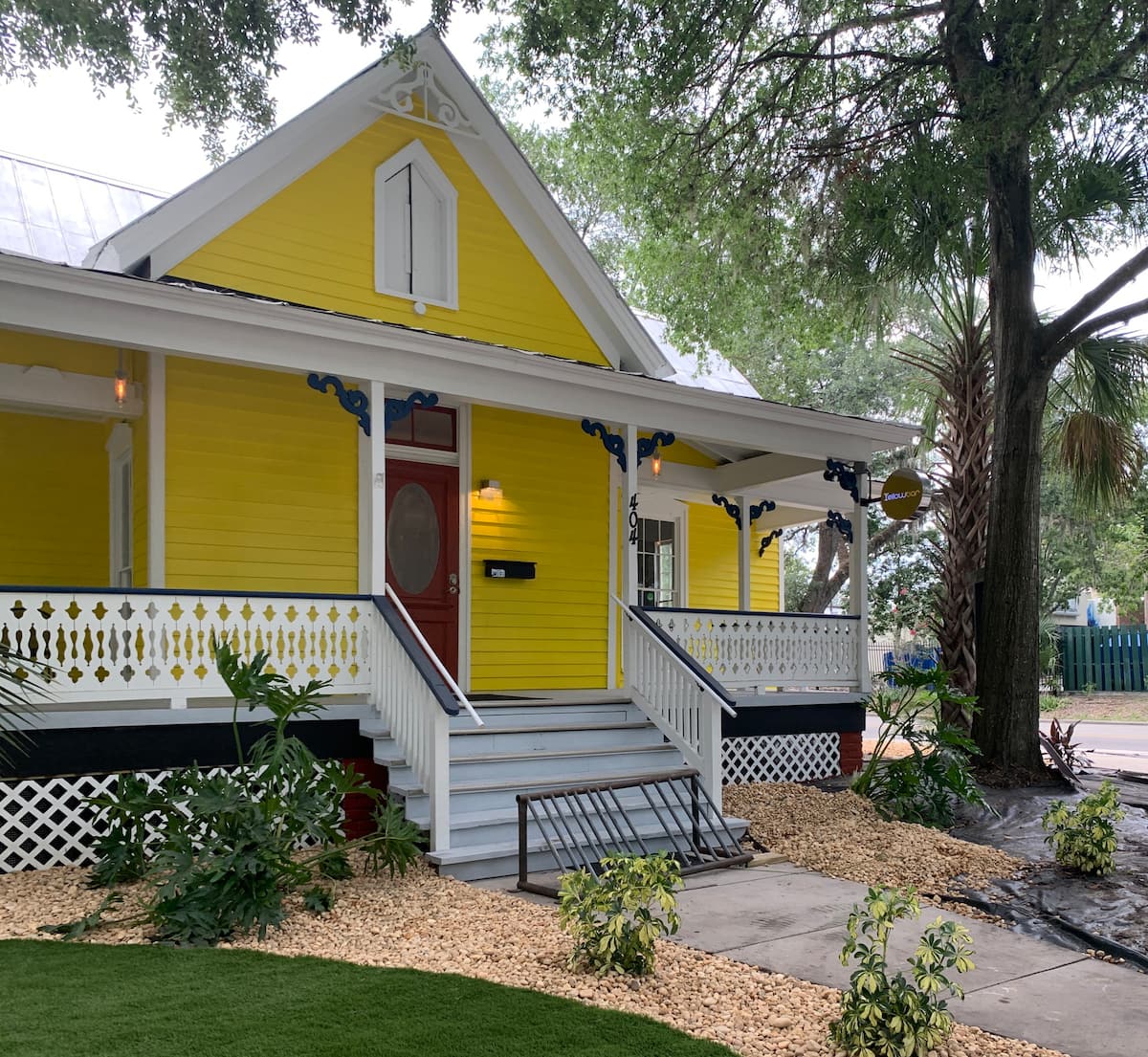 Yellow house with a porch, white trim, and red door. Landscaping includes gravel and a tree.