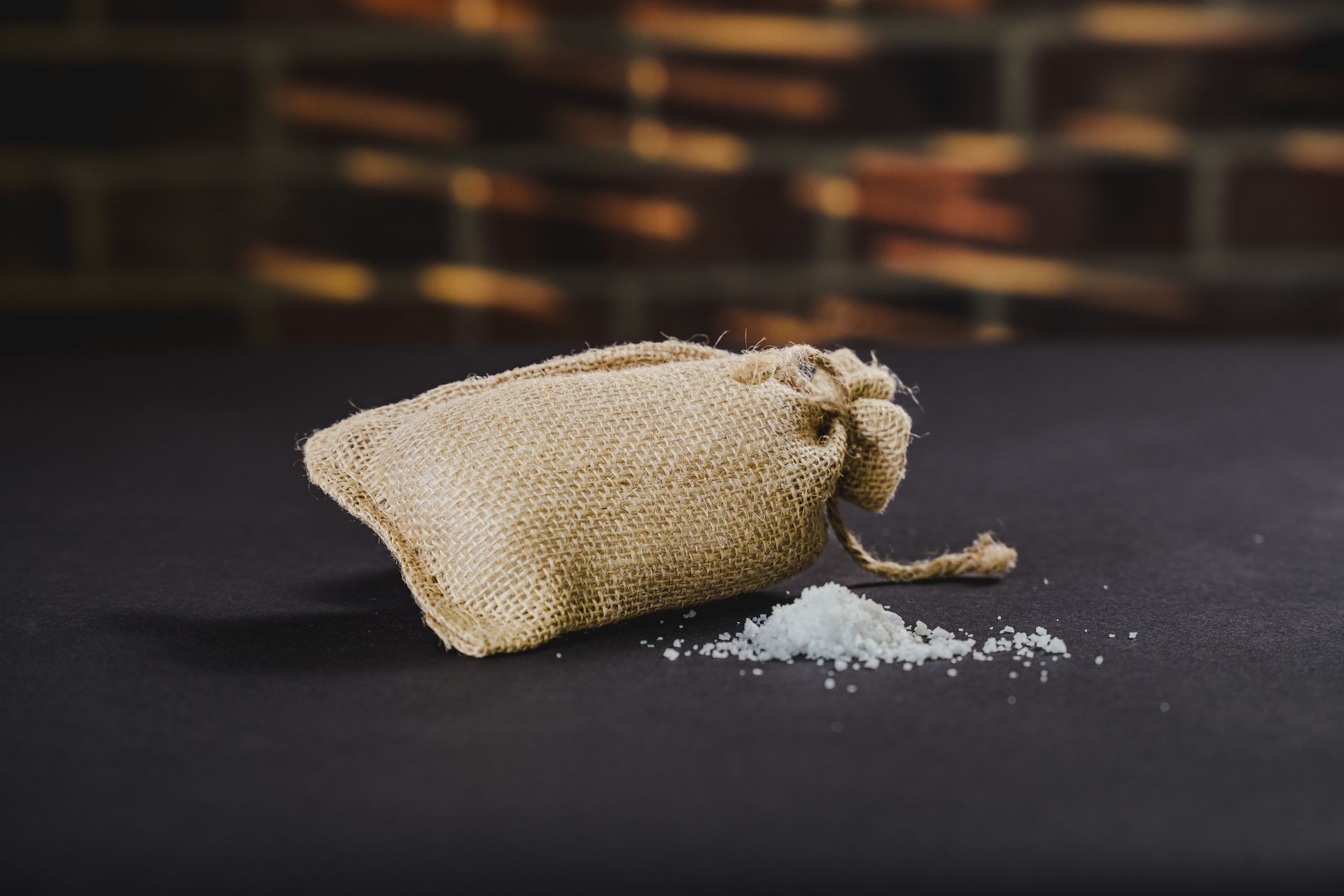 Un cuenco de madera con sal blanca gruesa sobre una mesa rústica, con coloridos pimientos y hierbas aromáticas cerca.