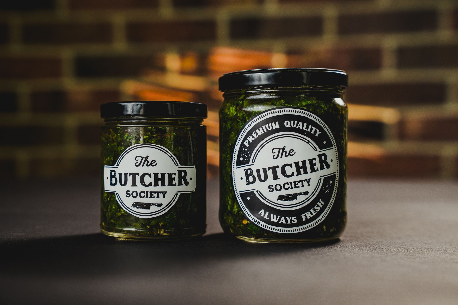 Chimichurri en un plato de cristal con una cuchara sobre una tabla de madera, rodeado de pan y alcachofas.