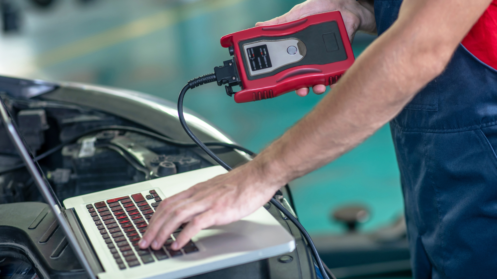 Mechanic using a red diagnostic scanner on a laptop beside an open car hood