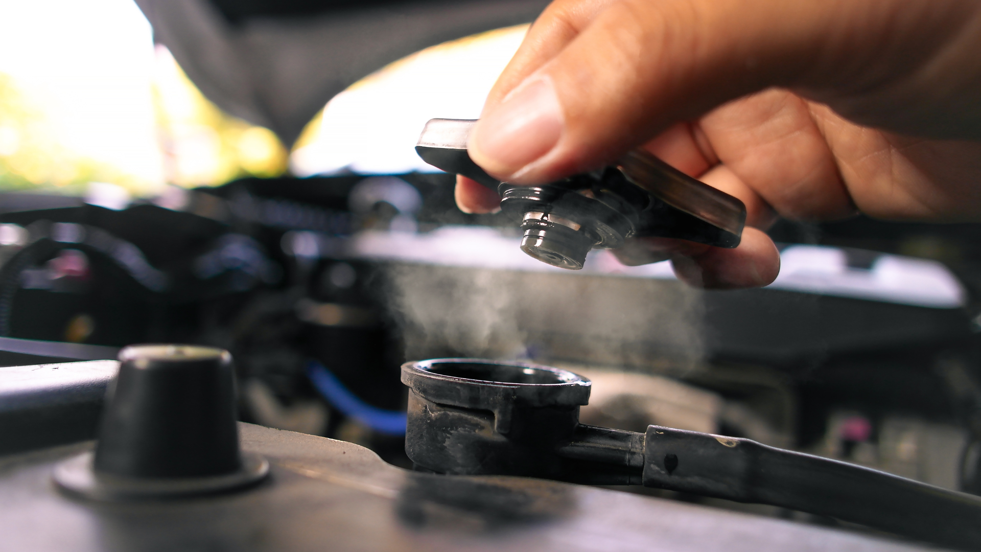 Hand holding a car battery cable clamp near an engine bay terminal