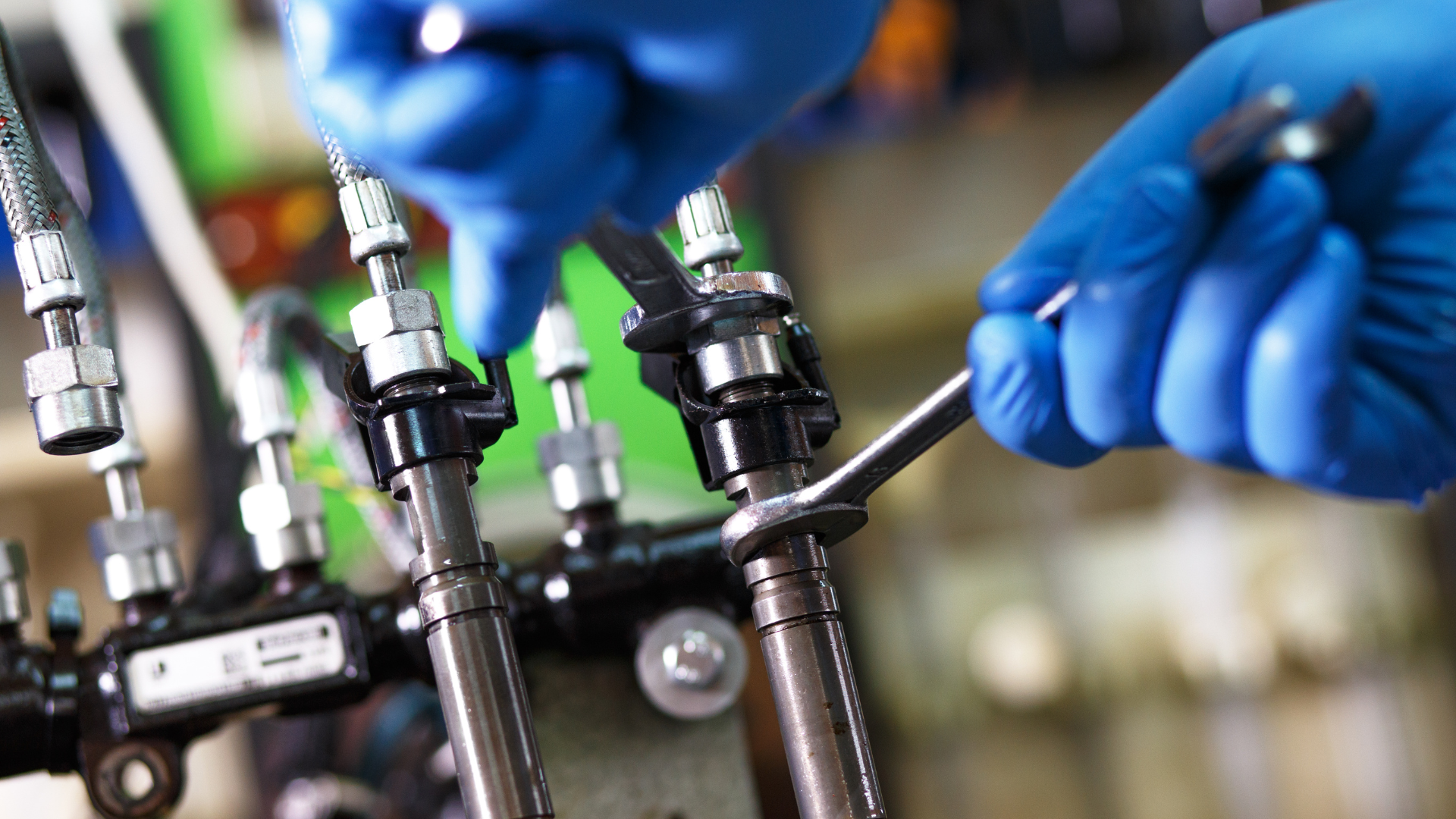 Blue-gloved hands adjust industrial valves and tubing on a production line, close-up.