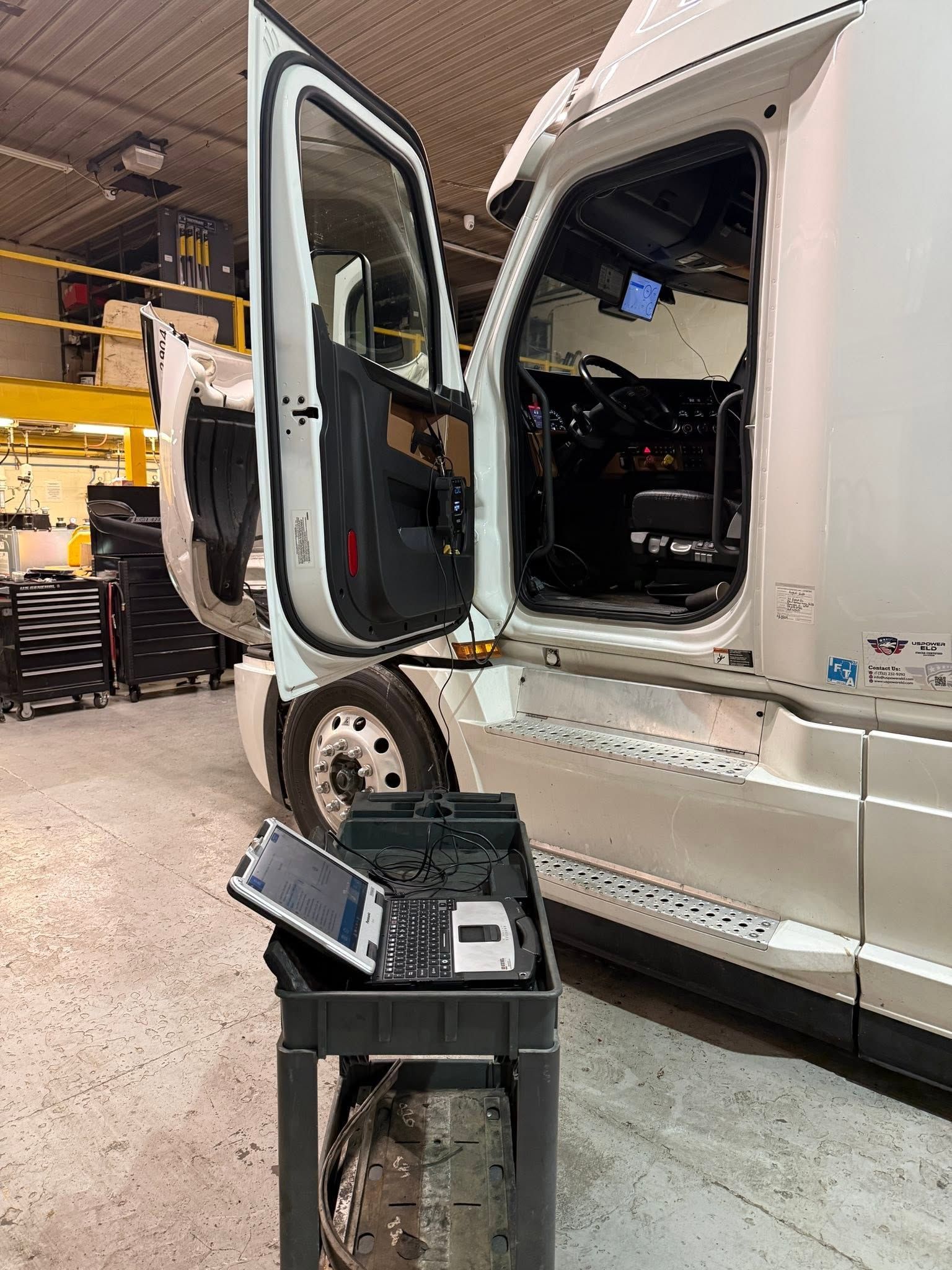 White semi-truck in a workshop with the door open beside a black equipment case on the floor