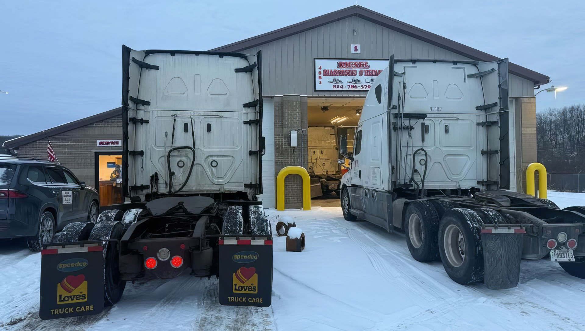 Two semi trucks back into a snowy warehouse loading dock at dusk.