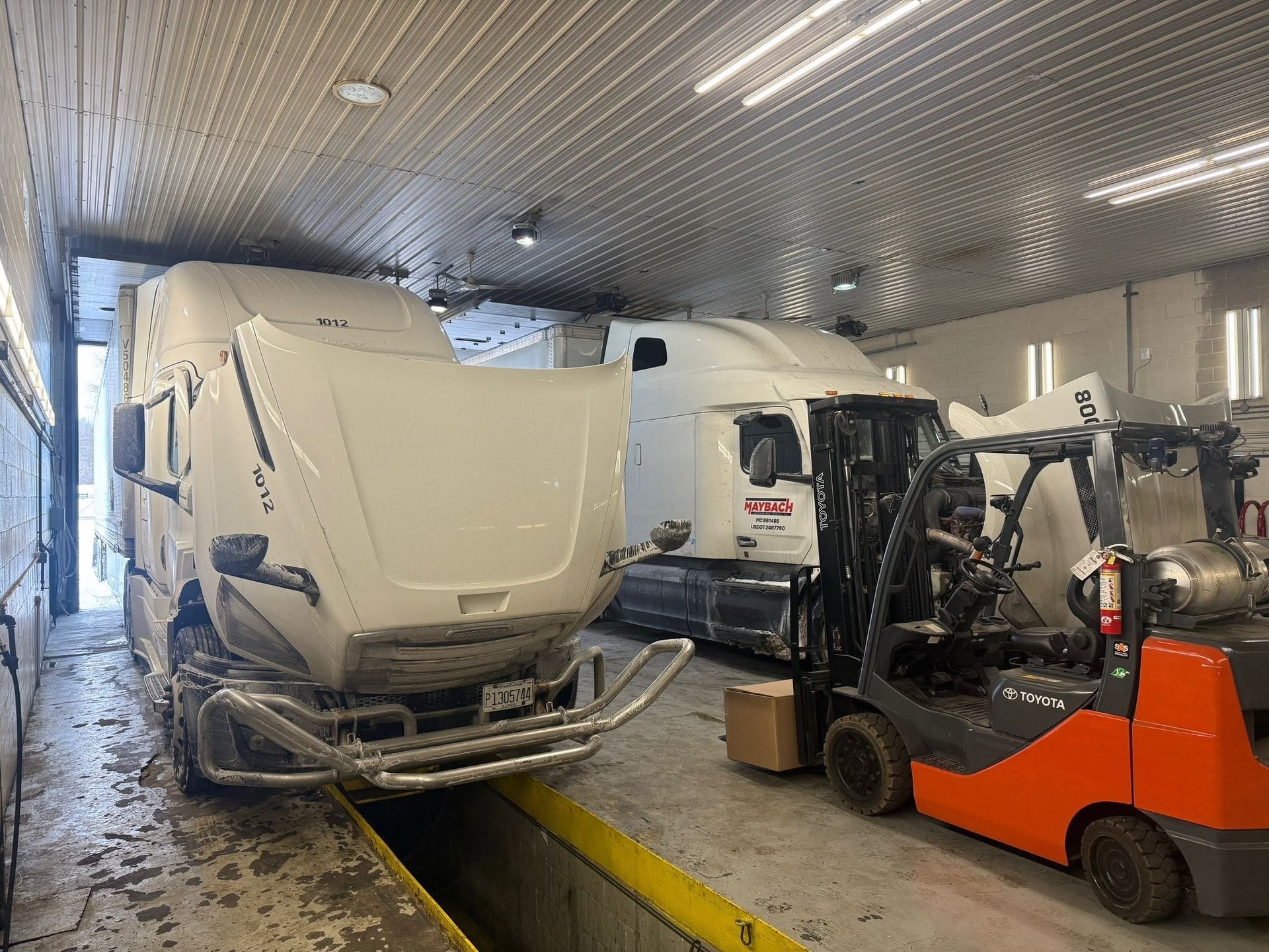 White semi-truck and orange forklift inside a loading bay, with a curved white cargo load in front