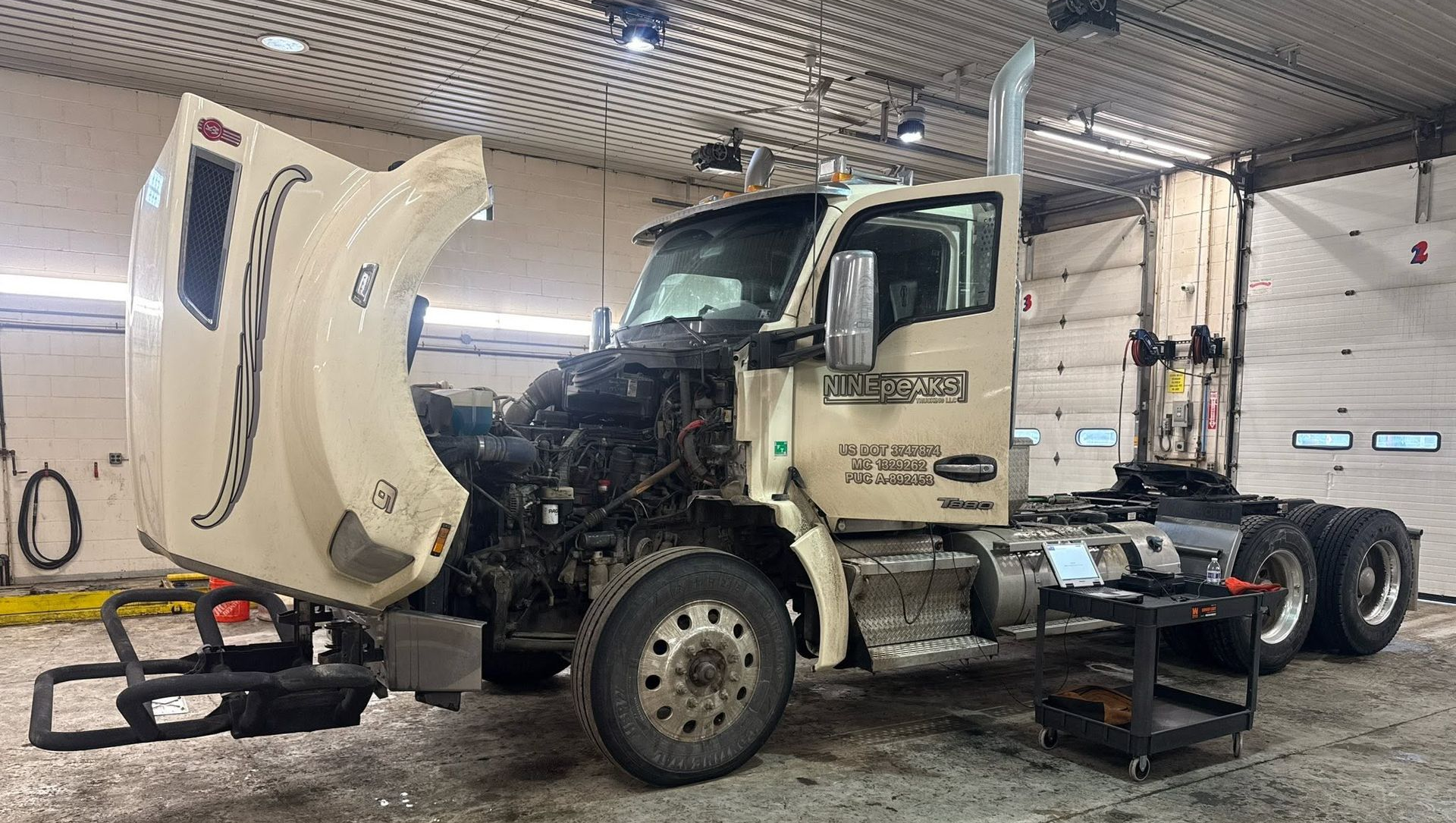 Semi-truck in a garage with hood open, undergoing maintenance on a lift rack