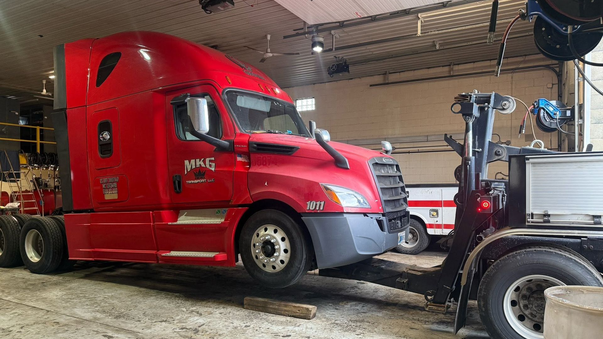 Red semi-truck parked nose-to-nose with a forklift inside a garage.