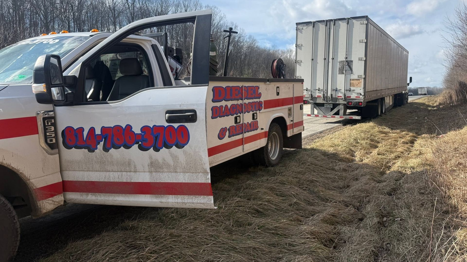 White utility truck with red stripes hauling a trailer in a grassy field under a cloudy sky