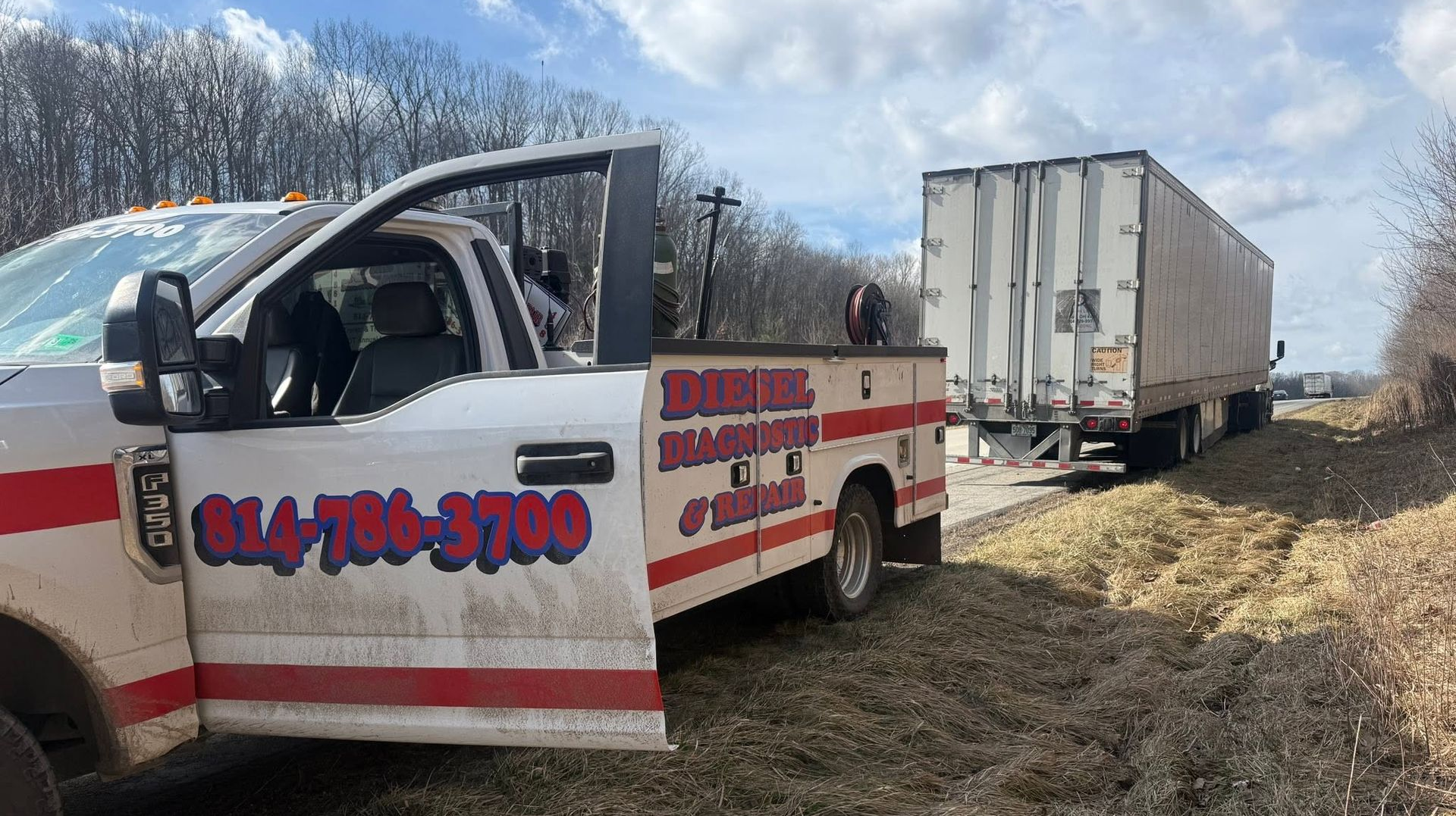 Tow truck with open door towing a white trailer on a muddy roadside in winter