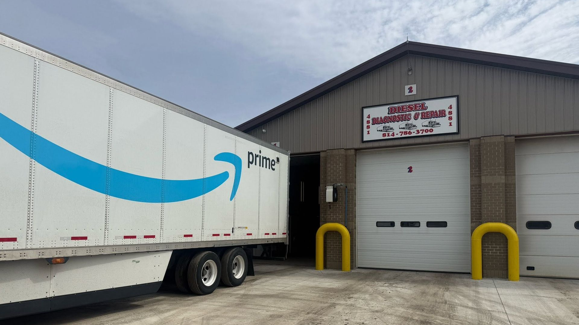 Amazon delivery truck at a warehouse loading dock with a closed garage door and yellow bollards