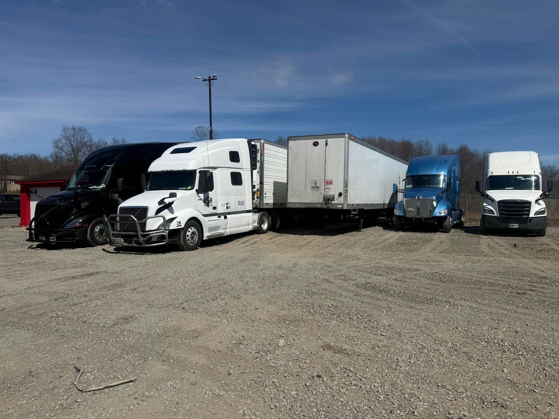 Several semi-trucks parked in a gravel lot under a clear blue sky