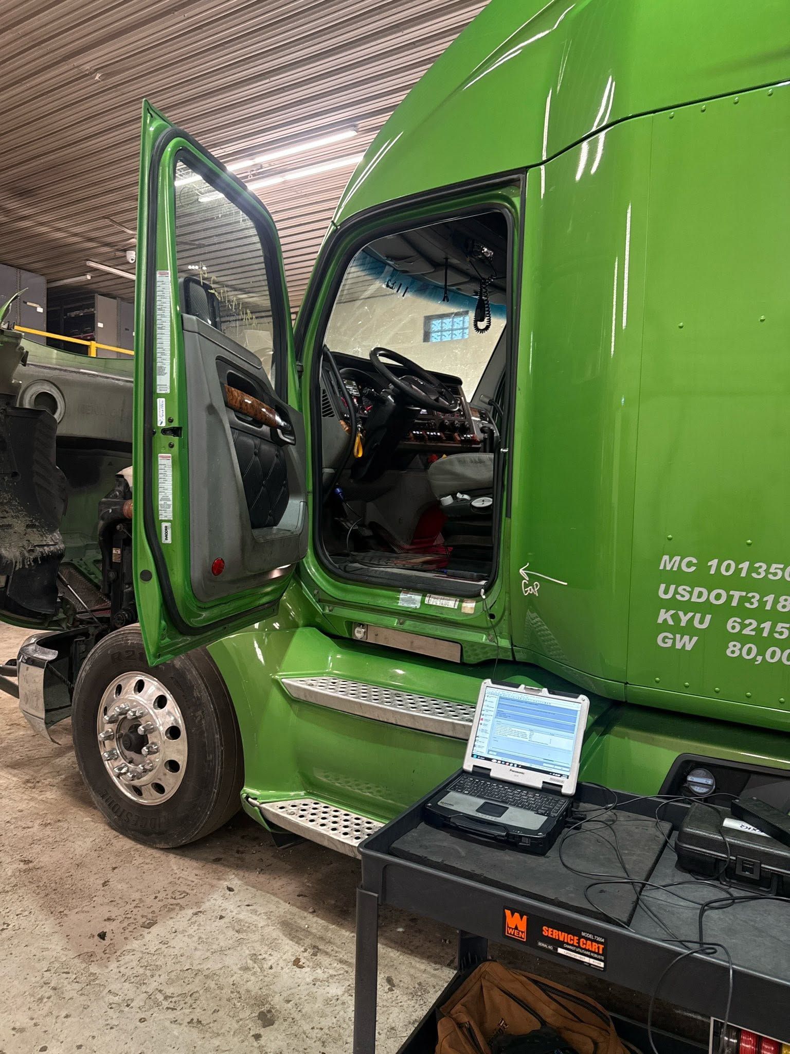 Green semi-truck in a workshop with the driver door open and a toolbox in front