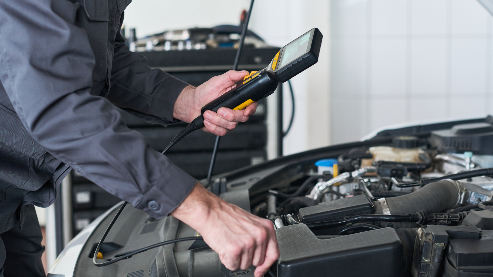 Mechanic using a handheld diagnostic scanner on a car engine in a garage