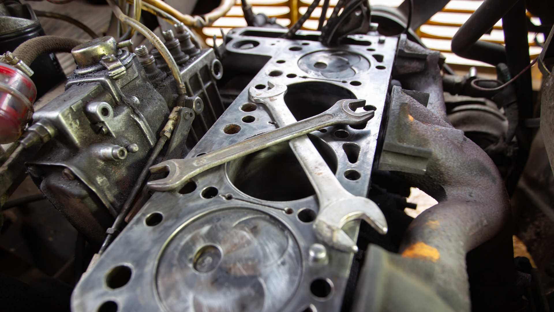 Close-up of a disassembled car engine with tools laid across the exposed cylinder head.