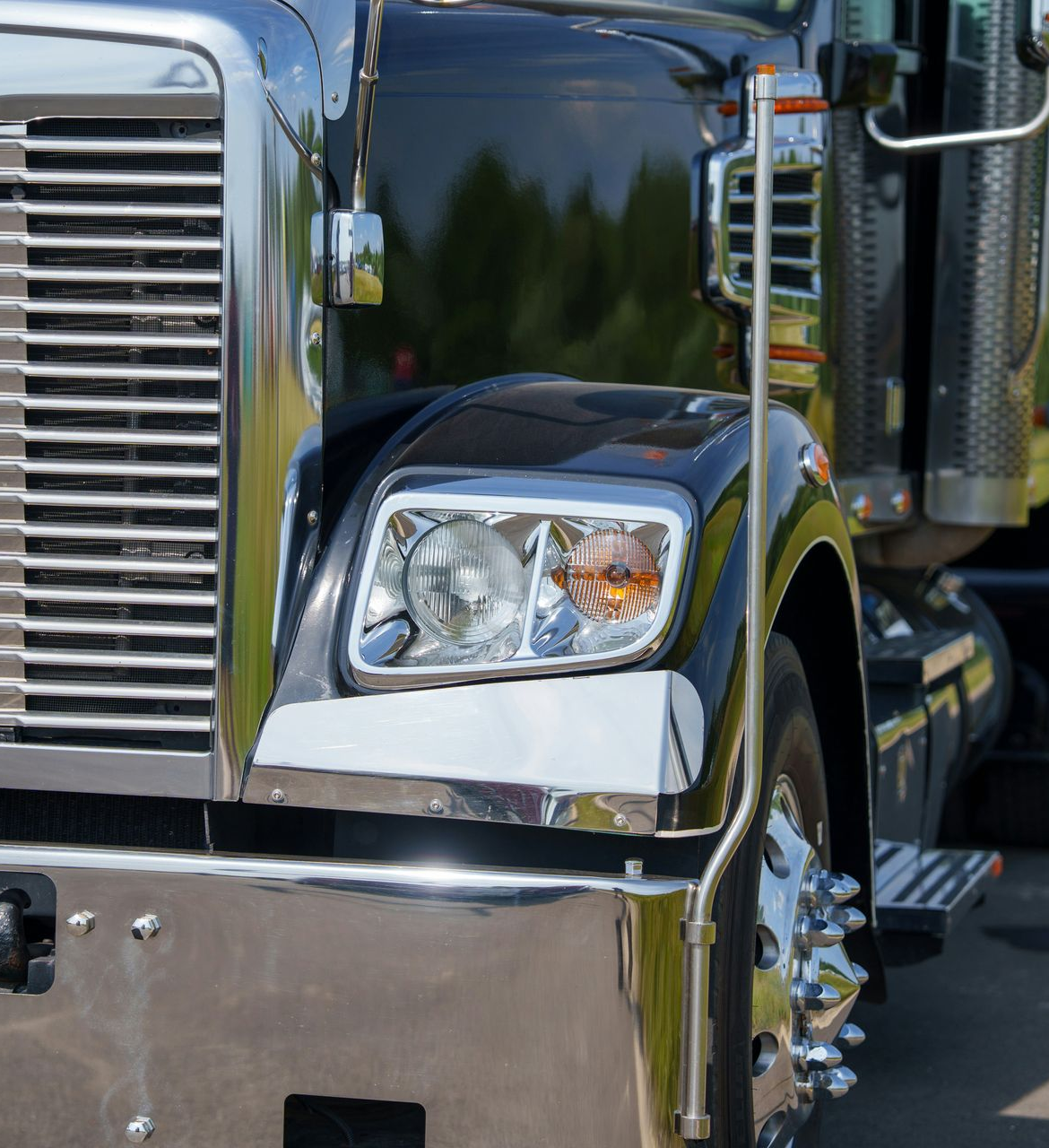 Close-up of a shiny black semi-truck front with chrome grille and headlight
