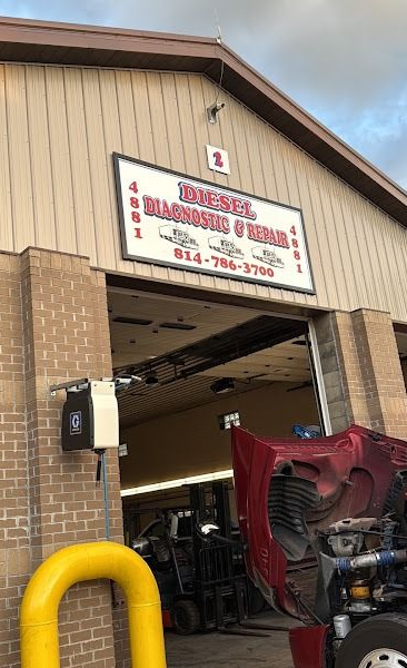 Auto body repair shop entrance with raised truck on a lift and red car hood in the bay