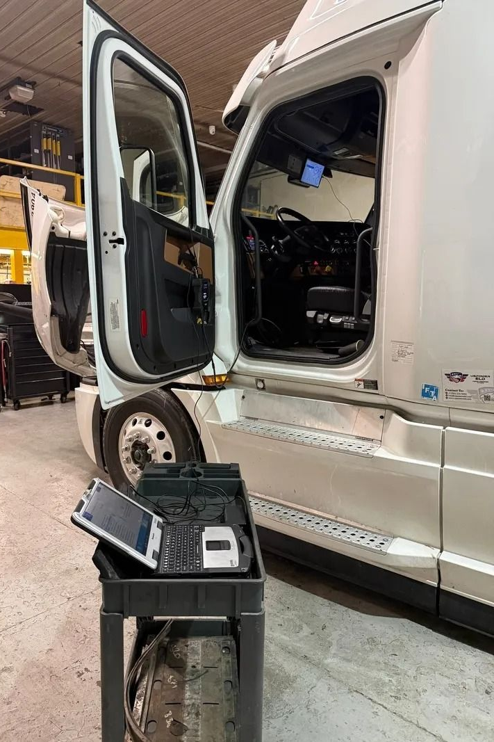 Open truck cab with doors ajar in a workshop, beside a portable tool cart.