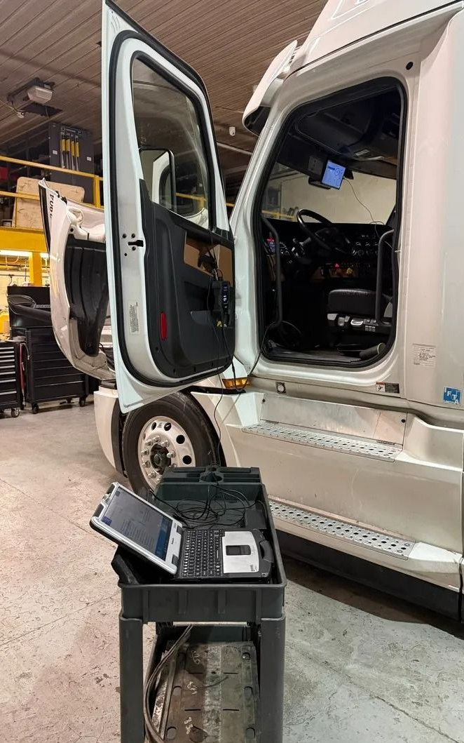 Open semi-truck cab at a repair shop with tools and equipment in the foreground