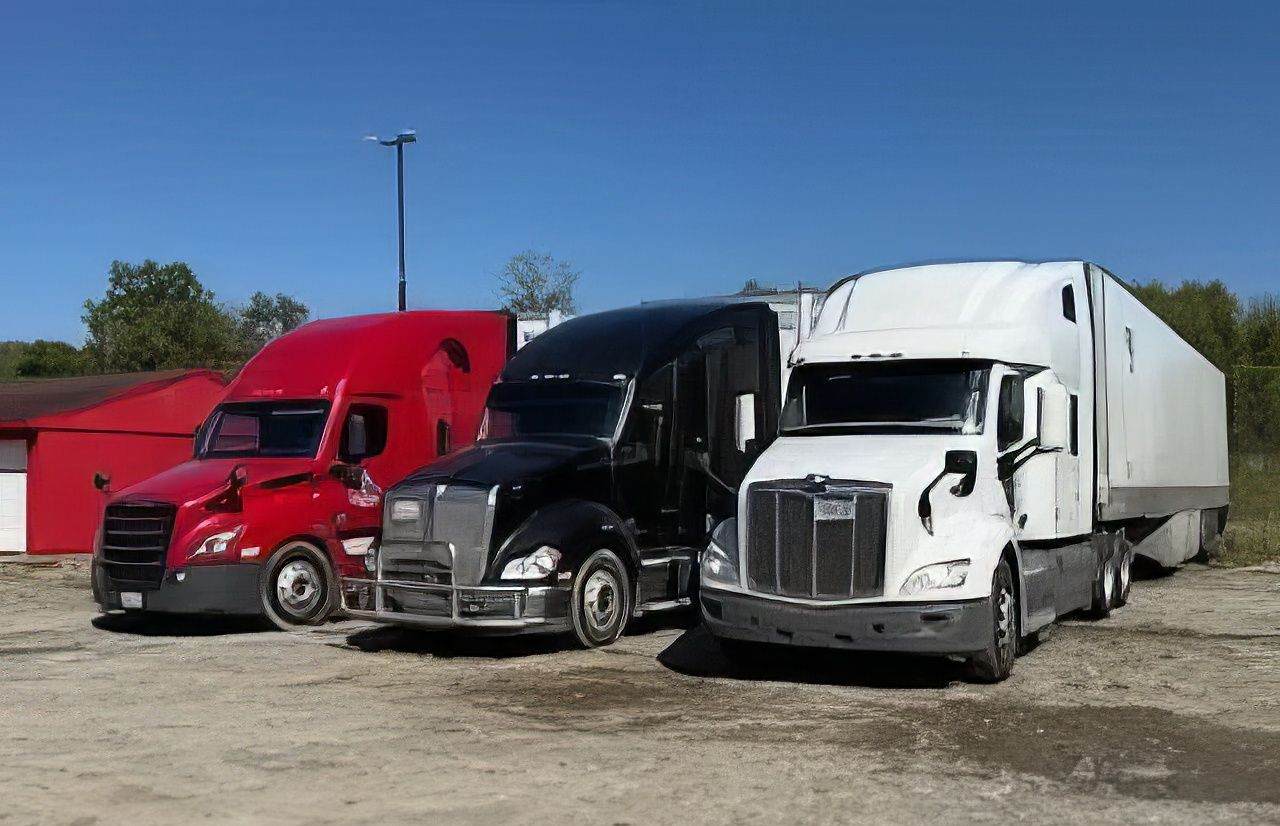 Three semi trucks parked side by side in a gravel lot under a blue sky