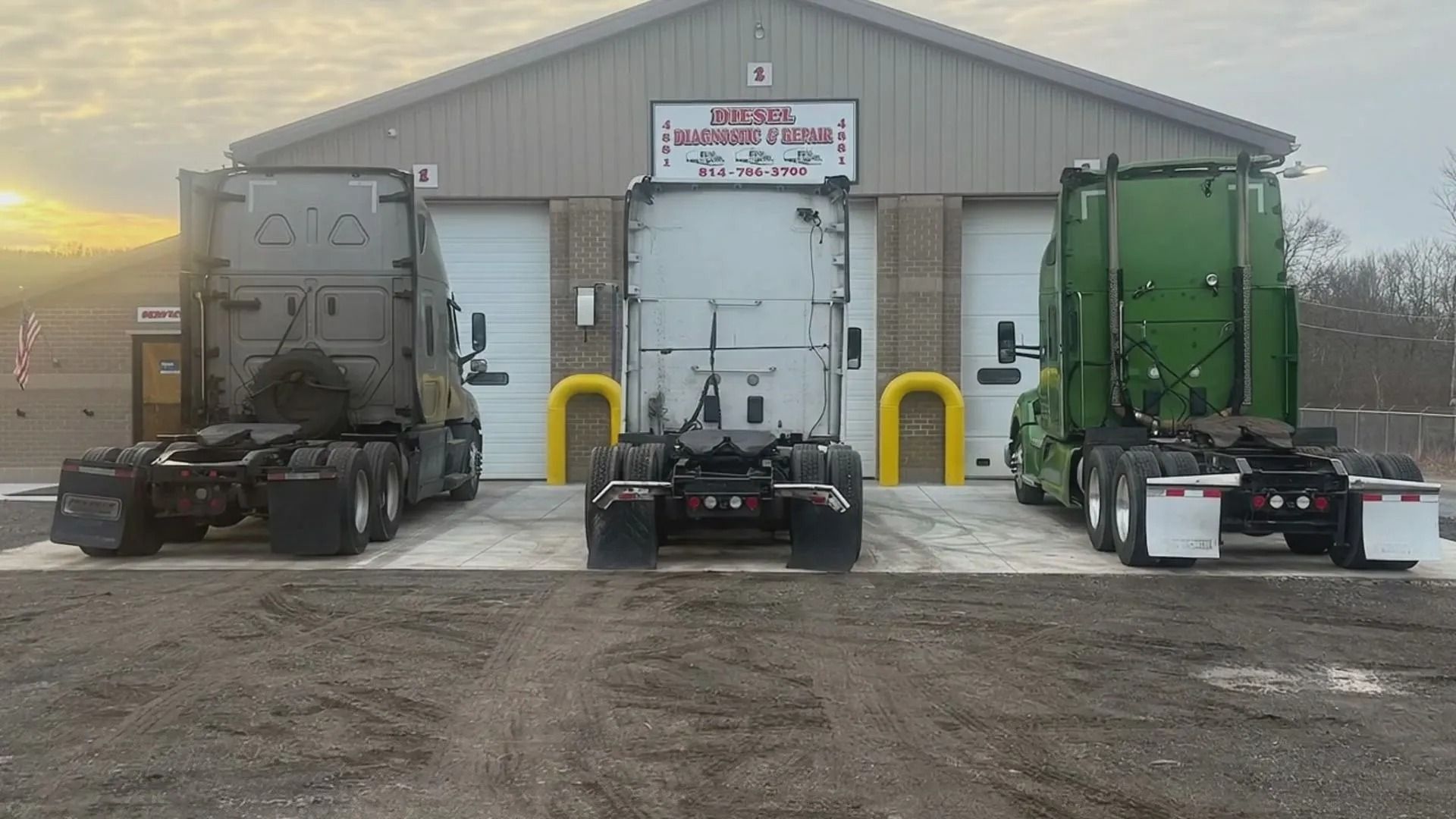 Three semi trucks parked in front of a warehouse, including black, white, and green cabs.
