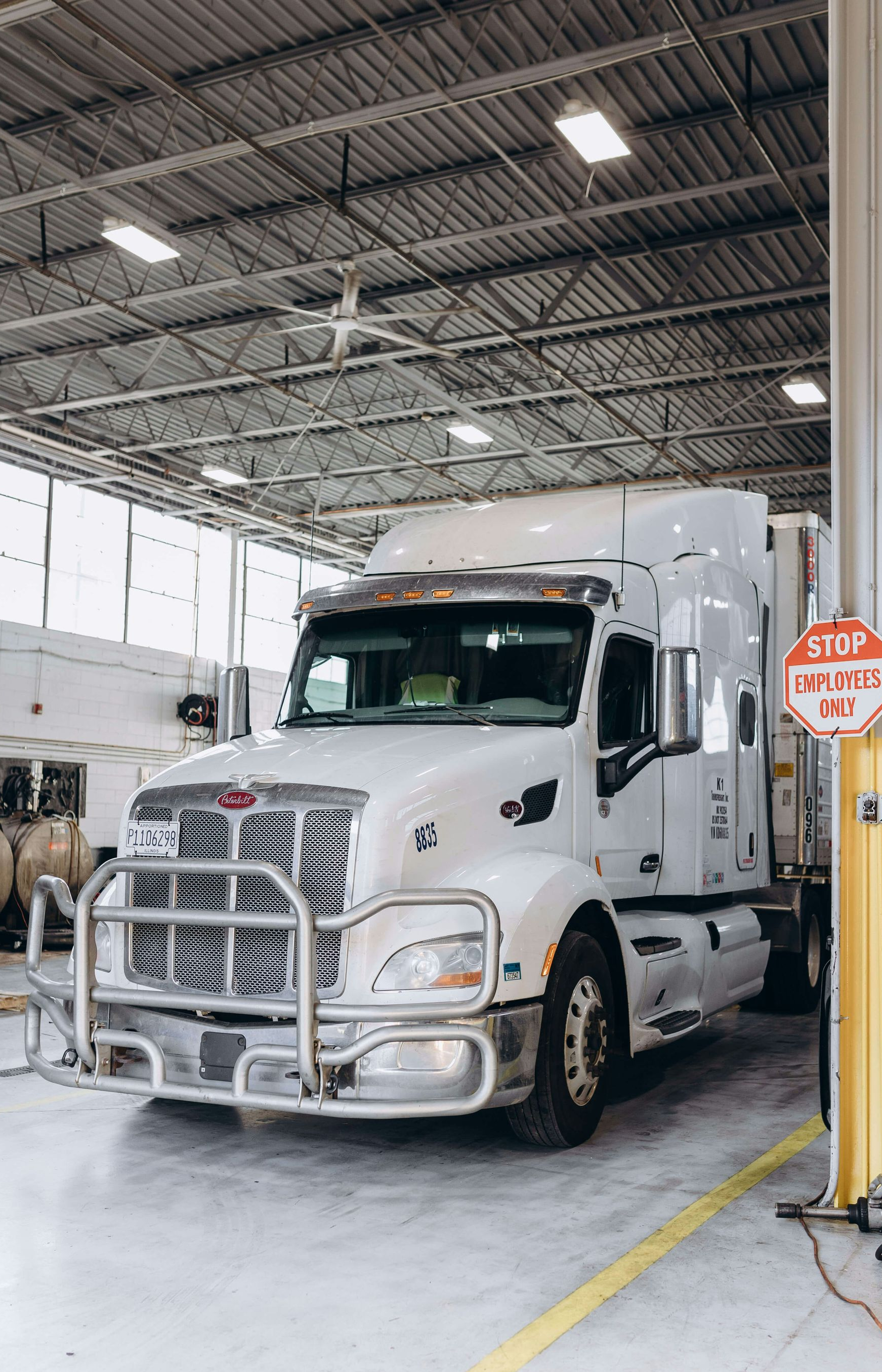 White semi-truck parked inside a bright maintenance garage near a service bay