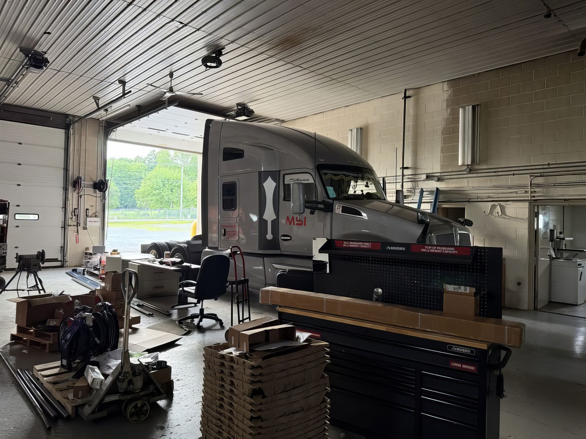 Semi-truck inside a garage with tools, equipment, and stacked parts around it
